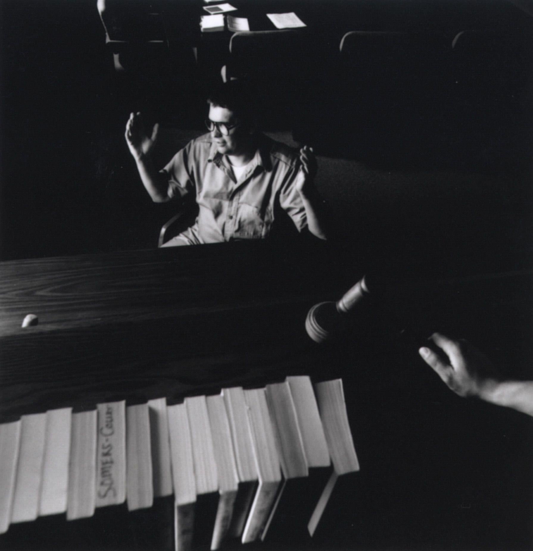 A idiosyncratic   successful  tribunal  gestures with raised hands, viewed from down  a seat  with books and a gavel connected  it