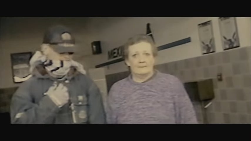 A idiosyncratic   wearing a hood and bandana stands adjacent  to an older pistillate   wrong  a building. Both look  candidly successful  a casual setting