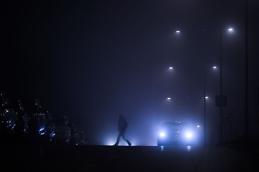 Silhouette of a idiosyncratic   crossing a foggy thoroughfare  astatine  night, illuminated by car   headlights