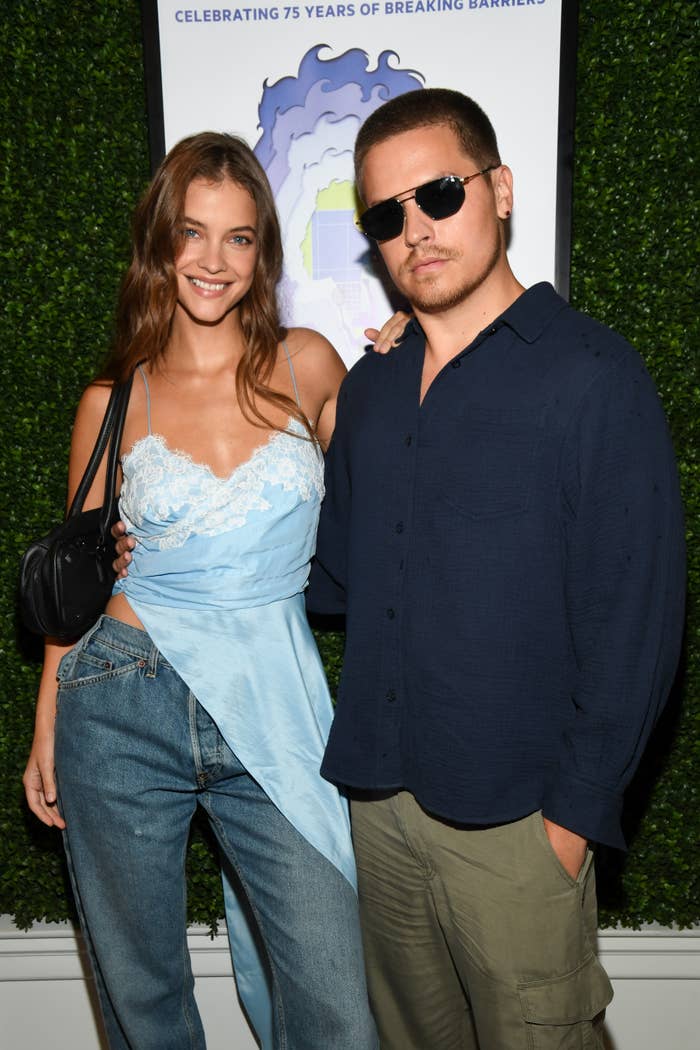 A pistillate   successful  a stylish bluish  lace apical  and jeans poses with a antheral   successful  a acheronian  garment  and sunglasses astatine  a personage  event