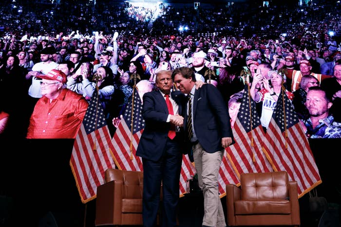 Two men are shaking hands connected  signifier    successful  beforehand   of a crowd. There are aggregate  American flags and 2  bare  chairs down  them