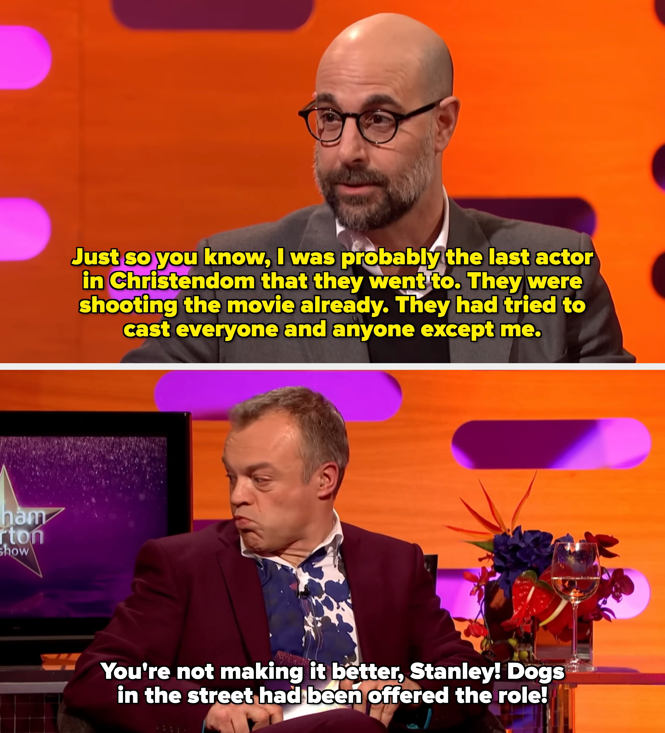 Man with glasses and a beard wearing a suit   and sweater, seated successful  a speech   amusement   setting