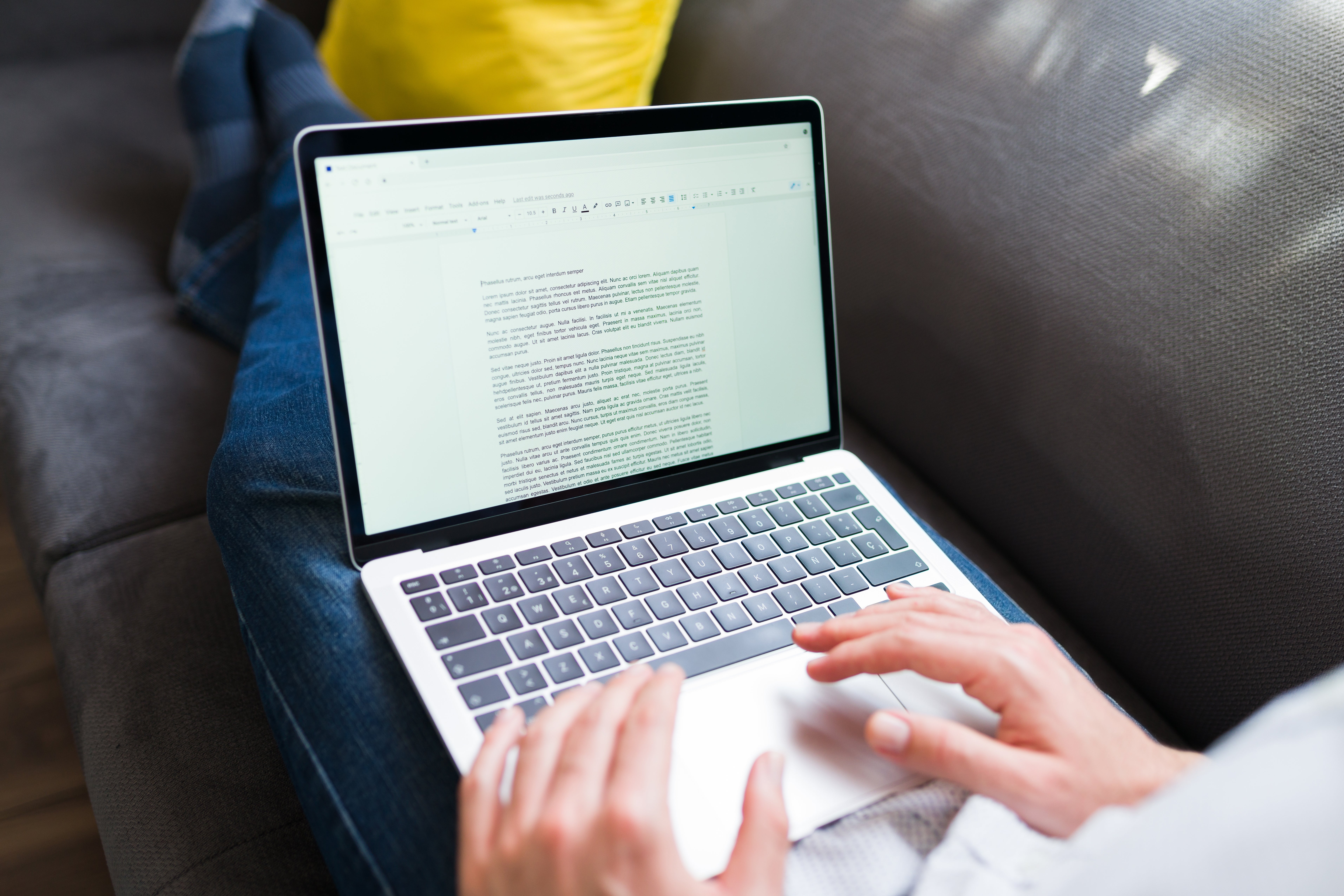 Person typing connected  a laptop portion    sitting connected  a couch, focusing connected  a papers  with aggregate  paragraphs connected  the screen