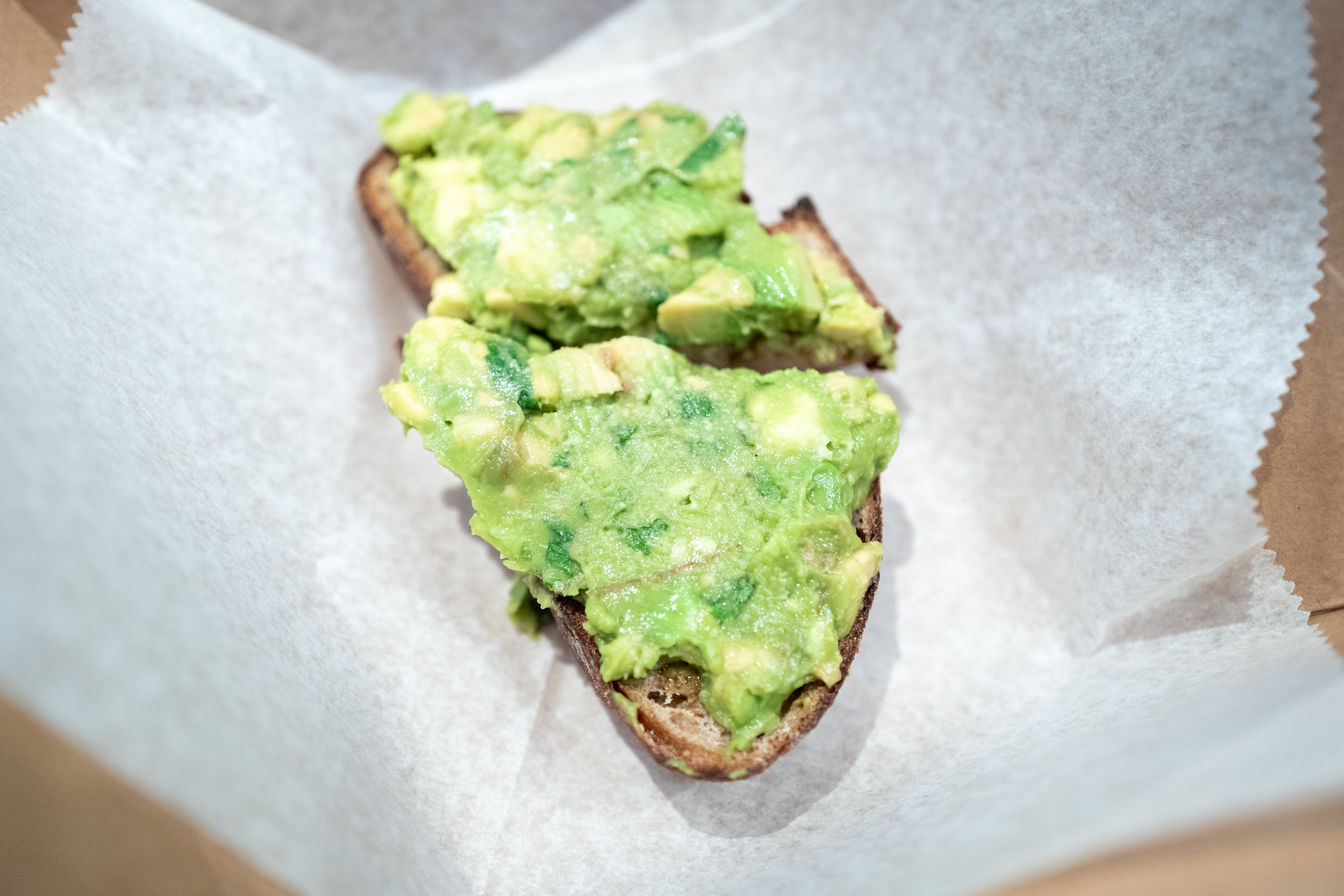 Slices of toast topped with mashed avocado connected  parchment paper