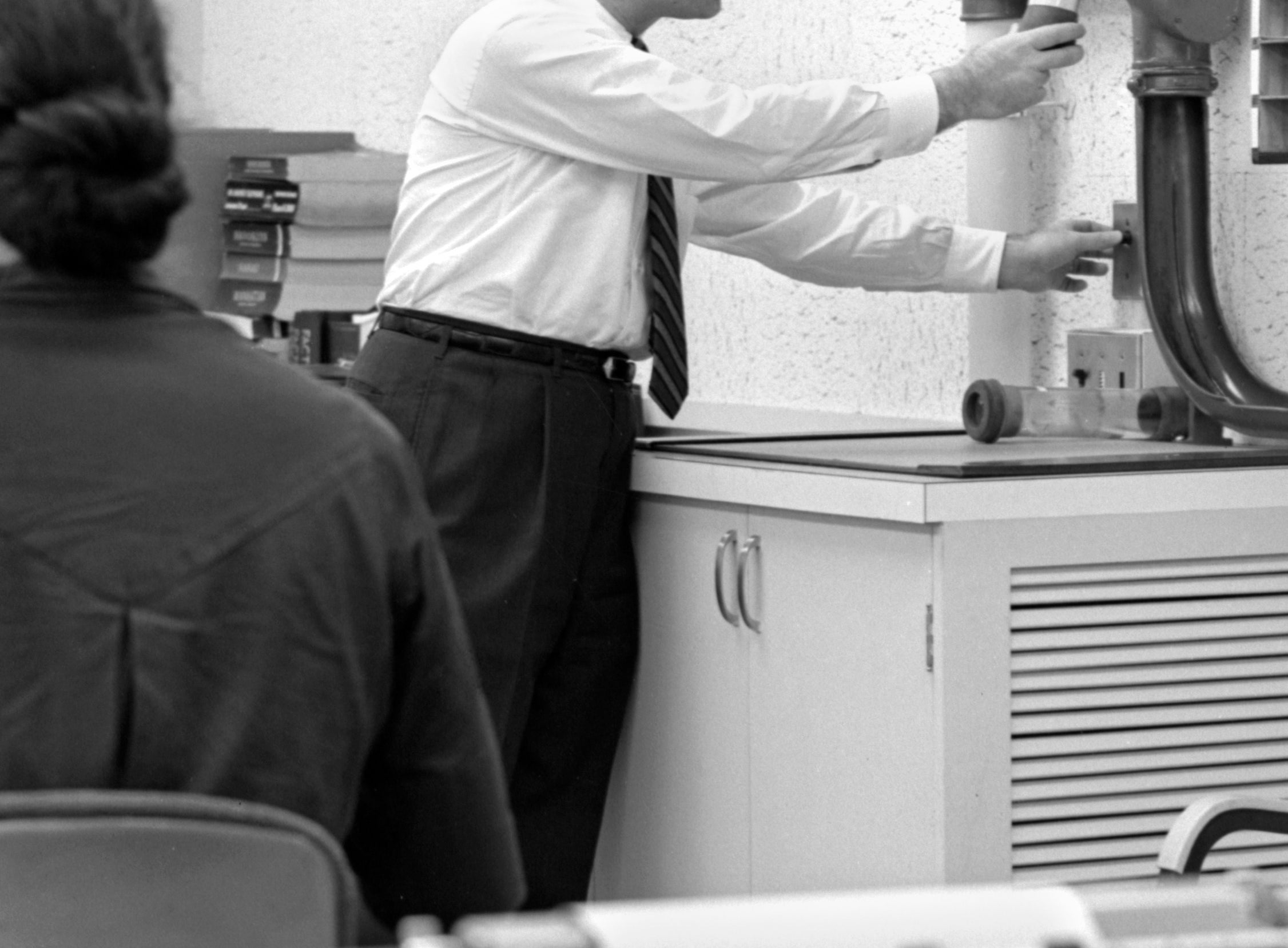 Office country   with a antheral   utilizing a pneumatic conduit  strategy   and a pistillate   seated astatine  a table  with a typewriter. Retro exertion   successful  a workspace