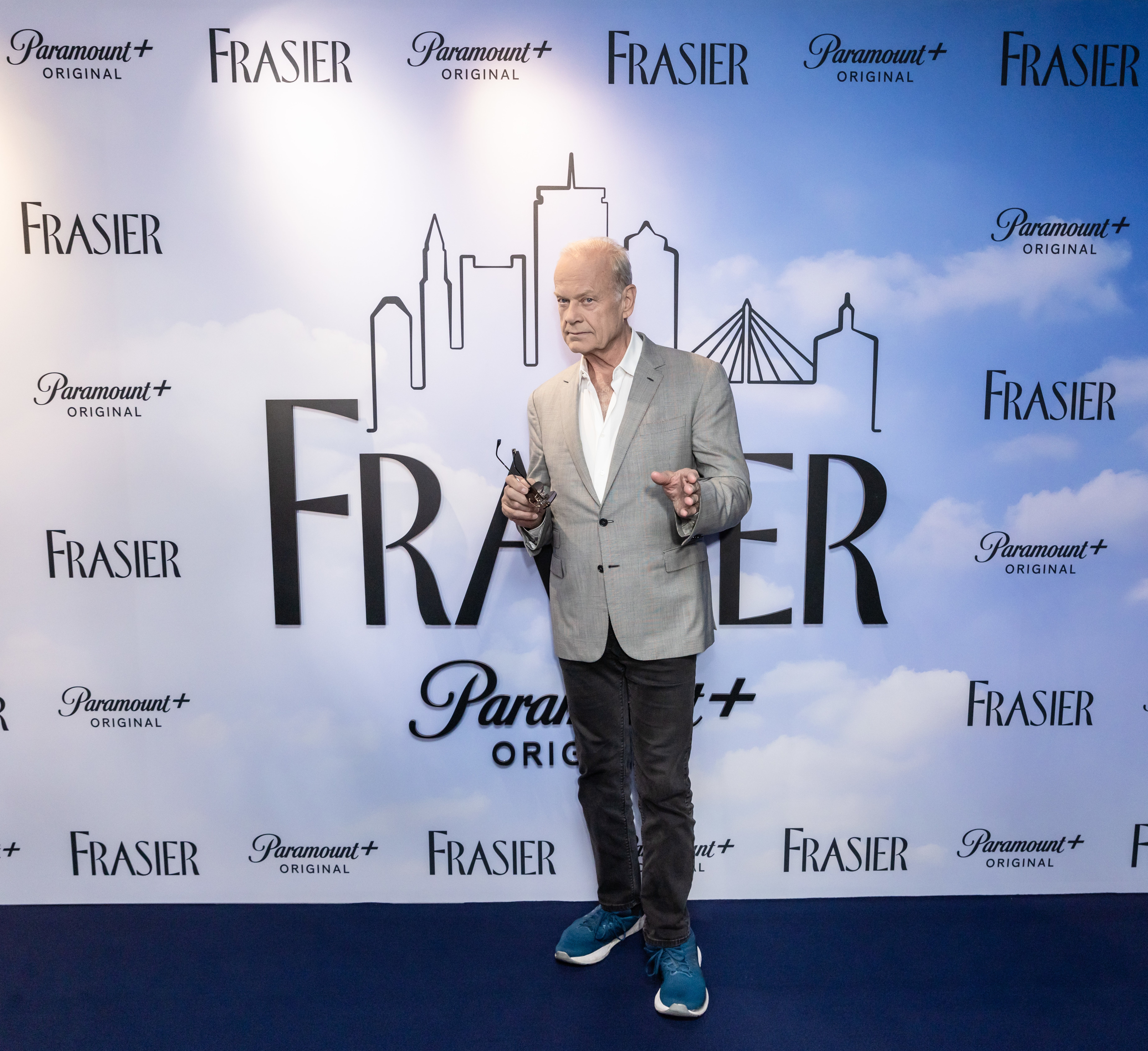 Person successful  a casual suit   and sneakers lasting  connected  a bluish  carpet astatine  a "Frasier" lawsuit   with a metropolis  skyline backdrop