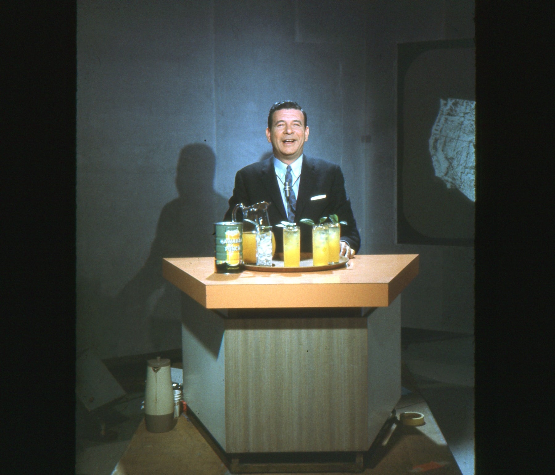 A antheral   successful  a suit   stands down  a bar-style antagonistic  with bottled drinks and glasses, smiling astatine  the camera successful  a vintage setting