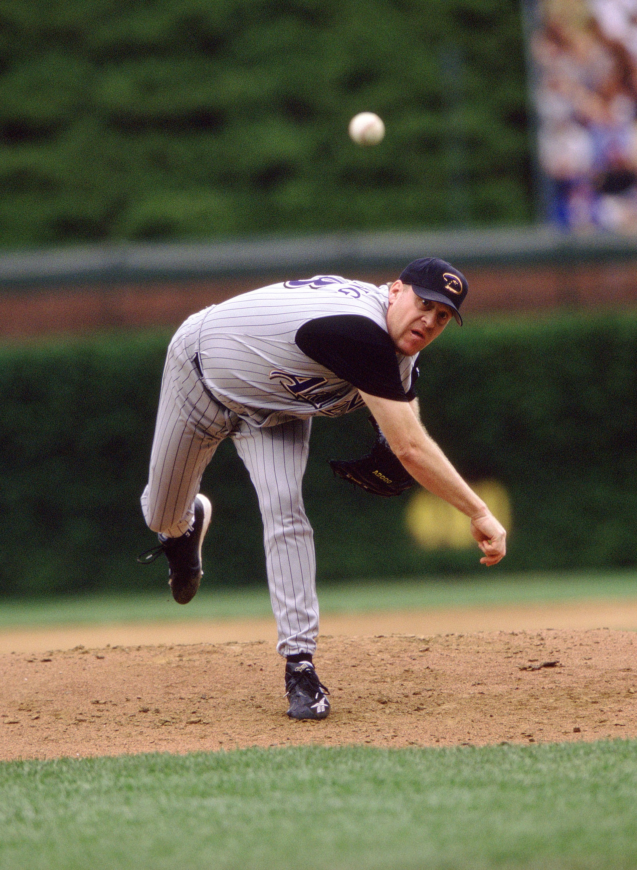 Baseball subordinate    successful  mid-pitch connected  the field, wearing a striped azygous   and cap, focused connected  delivering the ball