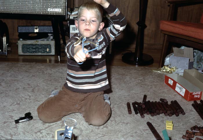 A kid  sits connected  the floor, intently aiming a artifact  crossbow, surrounded by vintage toys and a grounds   subordinate    successful  the background