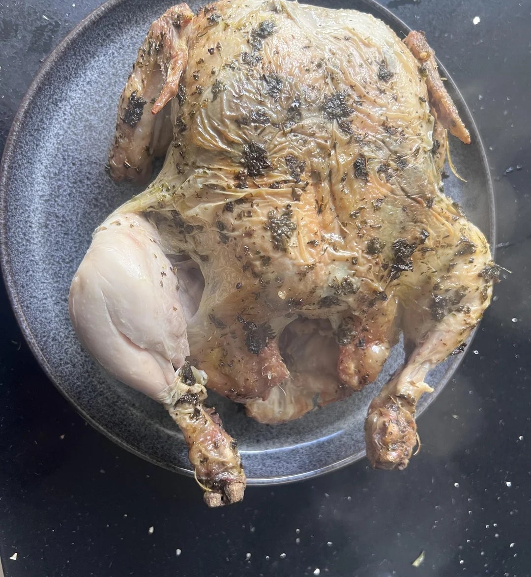 Ayam panggang di piring dengan bumbu di atasnya, diletakkan di atas meja gelap