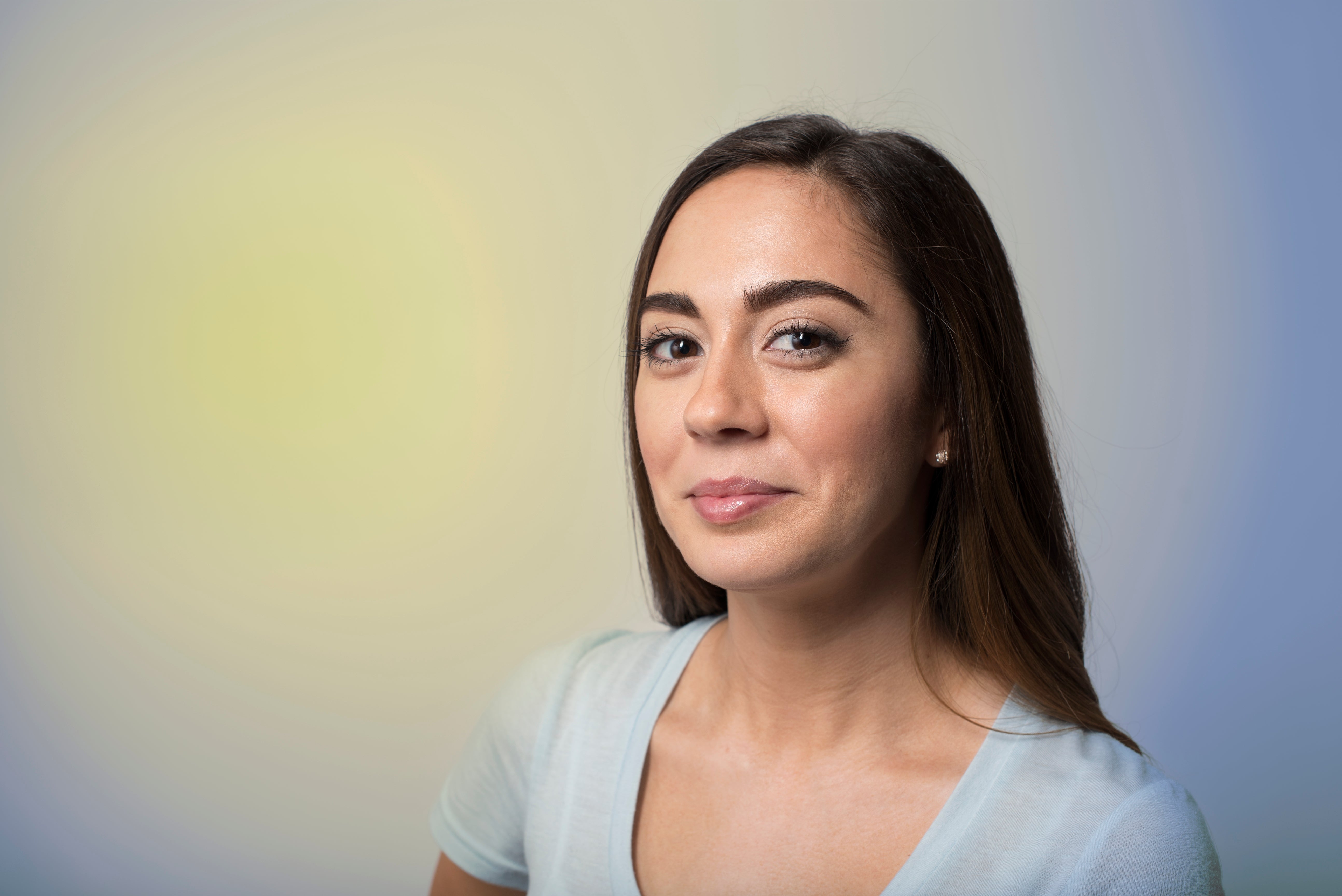 A pistillate   successful  a airy  apical  smiles subtly astatine  the camera with a neutral background