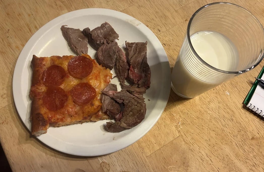 Piring dengan sepotong pizza pepperoni, beberapa potong irisan daging sapi, dan segelas susu di atas meja kayu