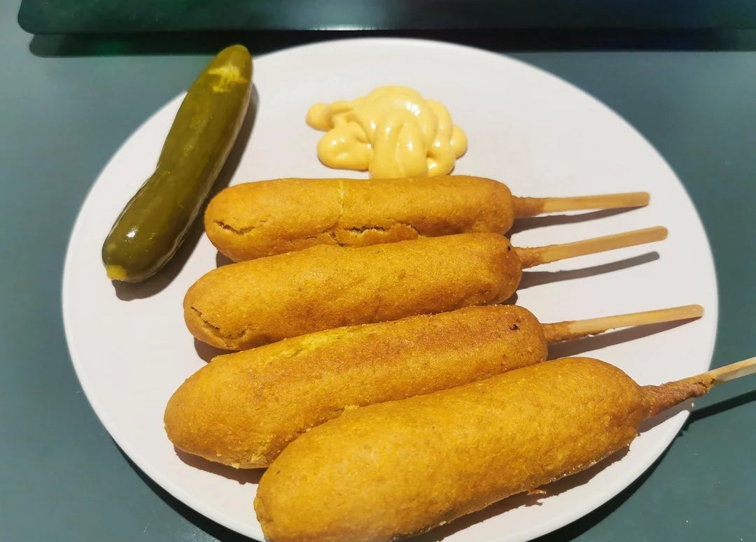 Piring dengan empat corn dog, acar, dan sesendok mustard di sampingnya