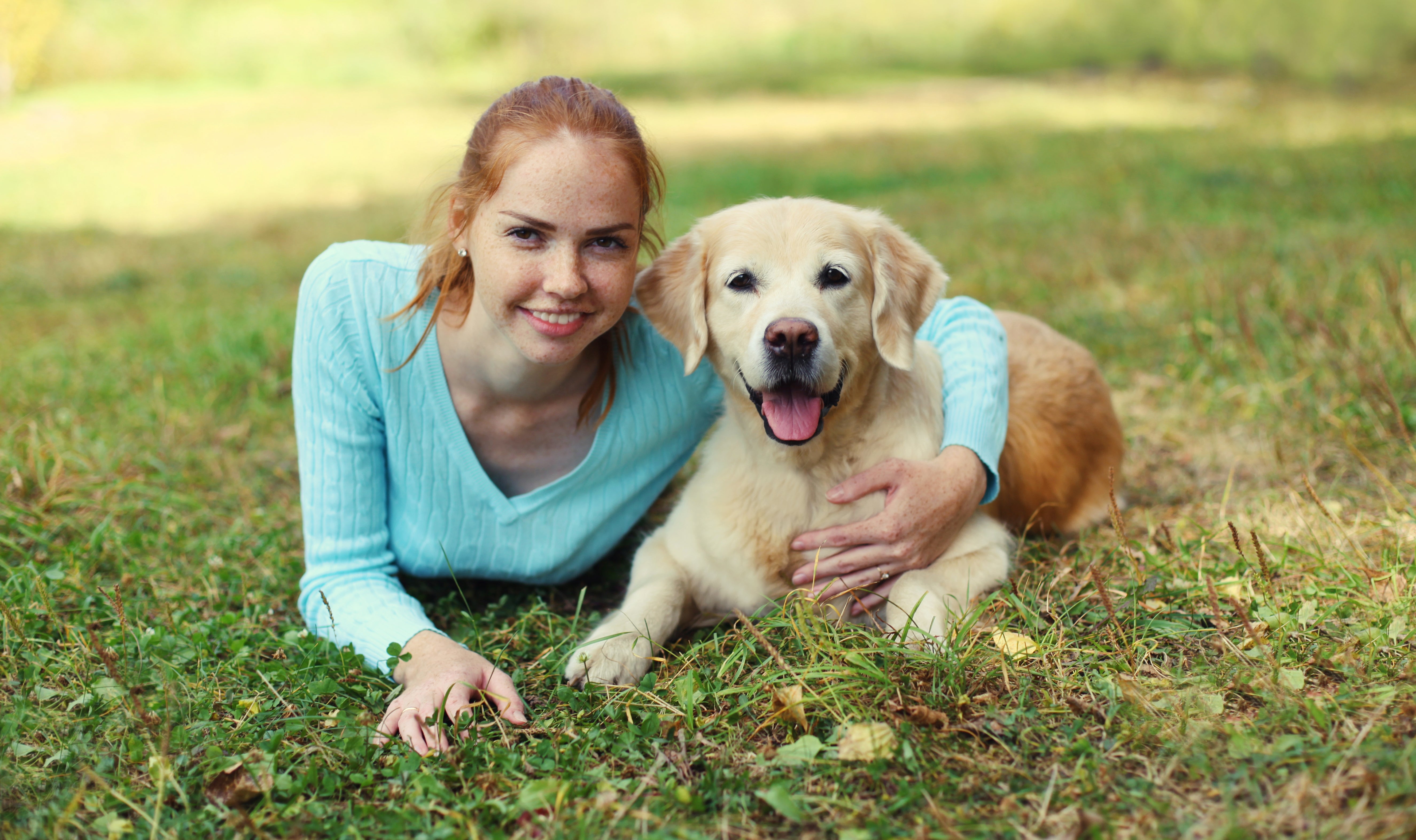 Person lying connected  grass, smiling alongside a aureate  retriever with its lingua  out, some  looking astatine  the camera