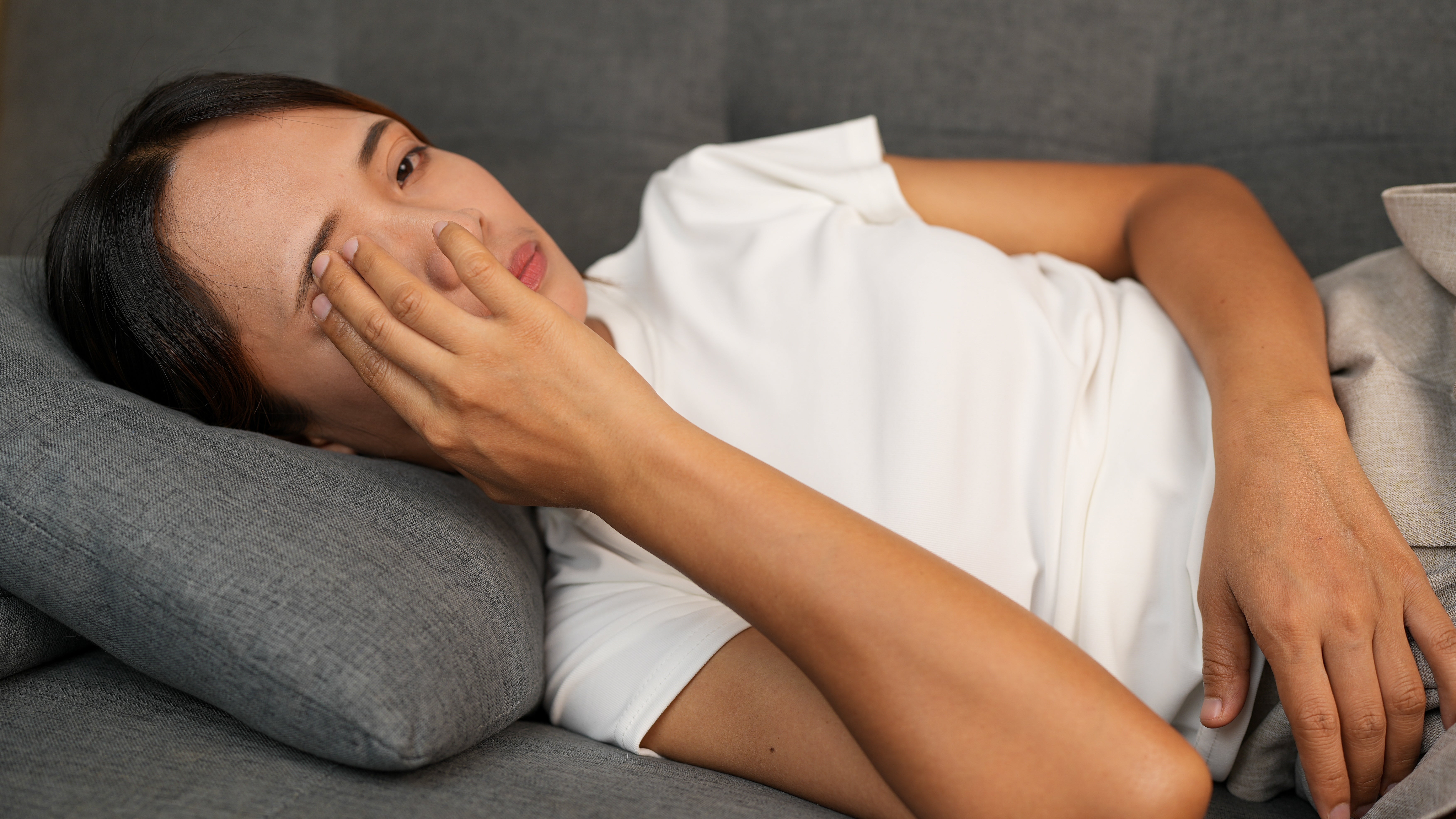 Person lying connected  a sofa  with 1  manus  covering their face, appearing bushed   oregon  contemplative, wearing a plain t-shirt