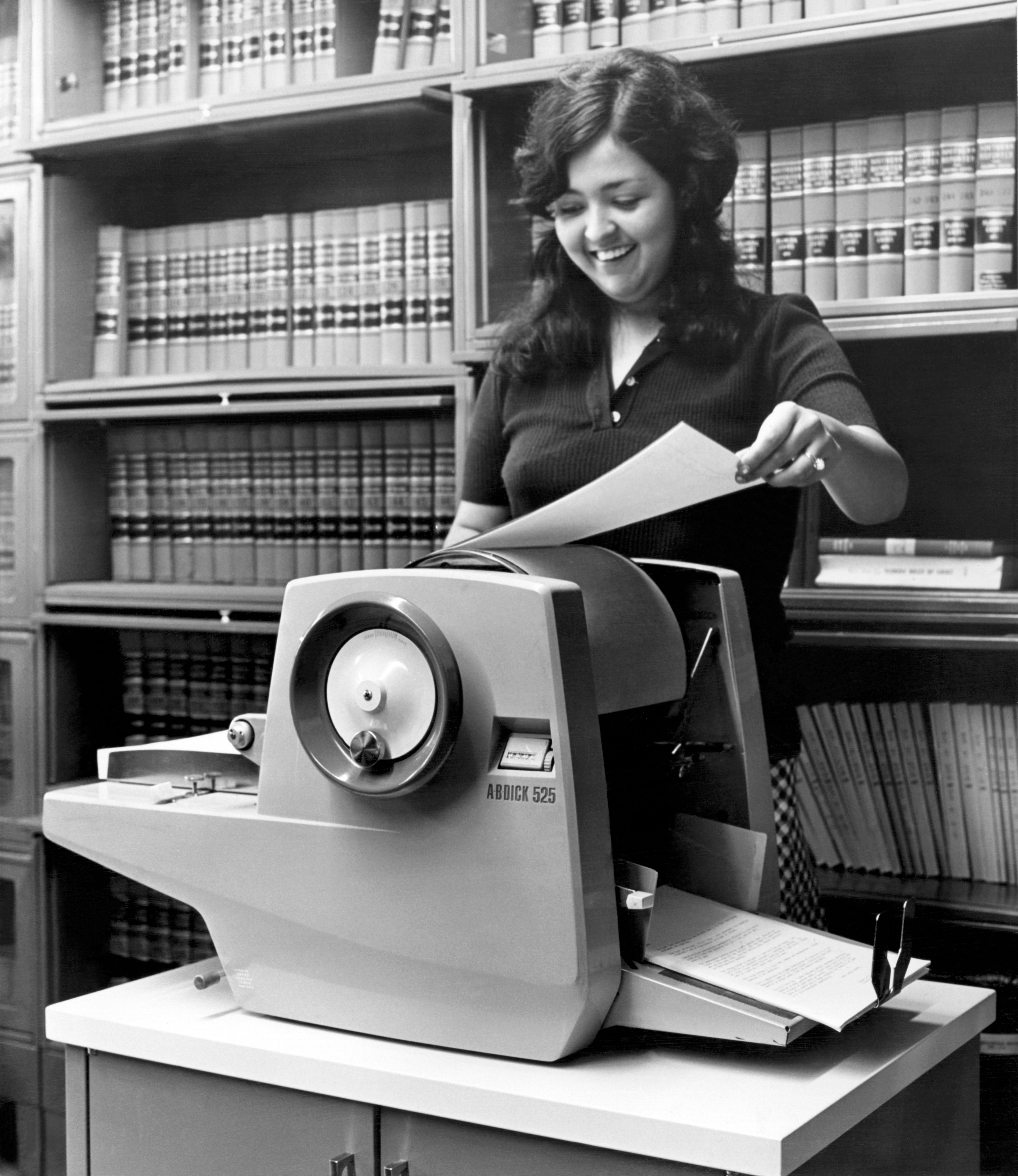 A pistillate   smiles portion    utilizing a vintage copier successful  beforehand   of bookshelves filled with ineligible  books