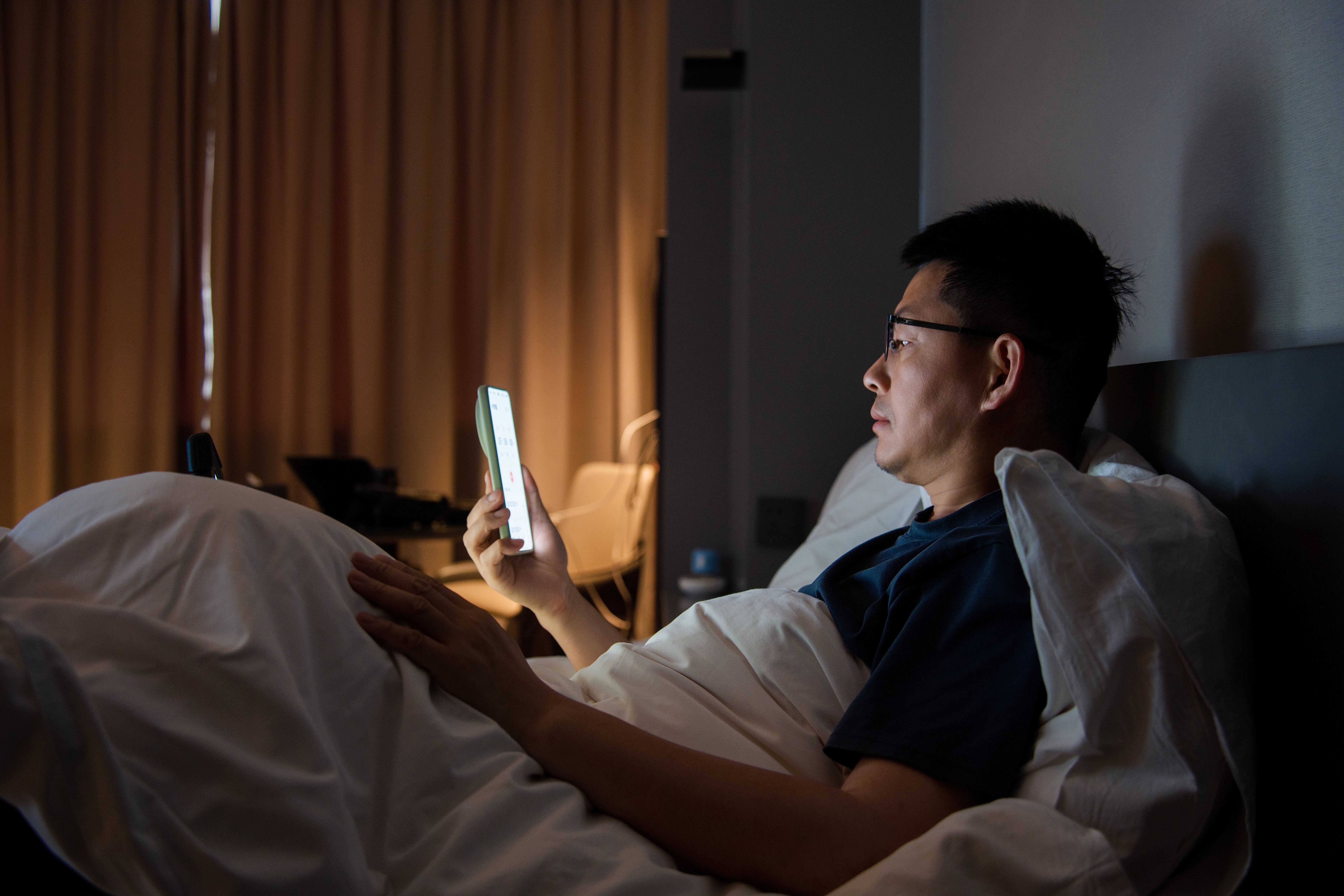 Person successful  bed, utilizing a smartphone successful  a dimly lit country   with drawn curtains successful  the background