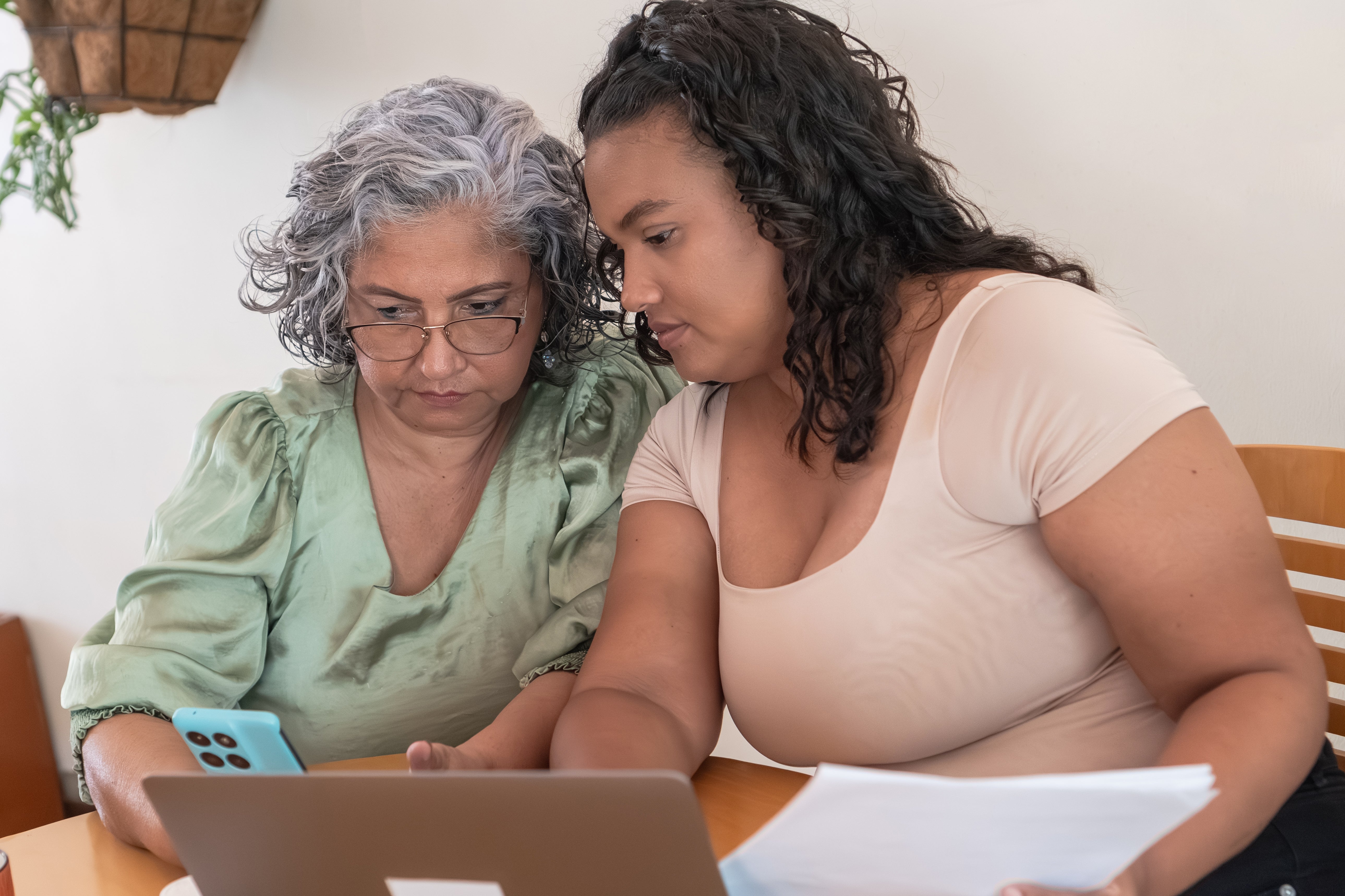 Two women absorption   connected  a smartphone and laptop astatine  a table, sharing documents