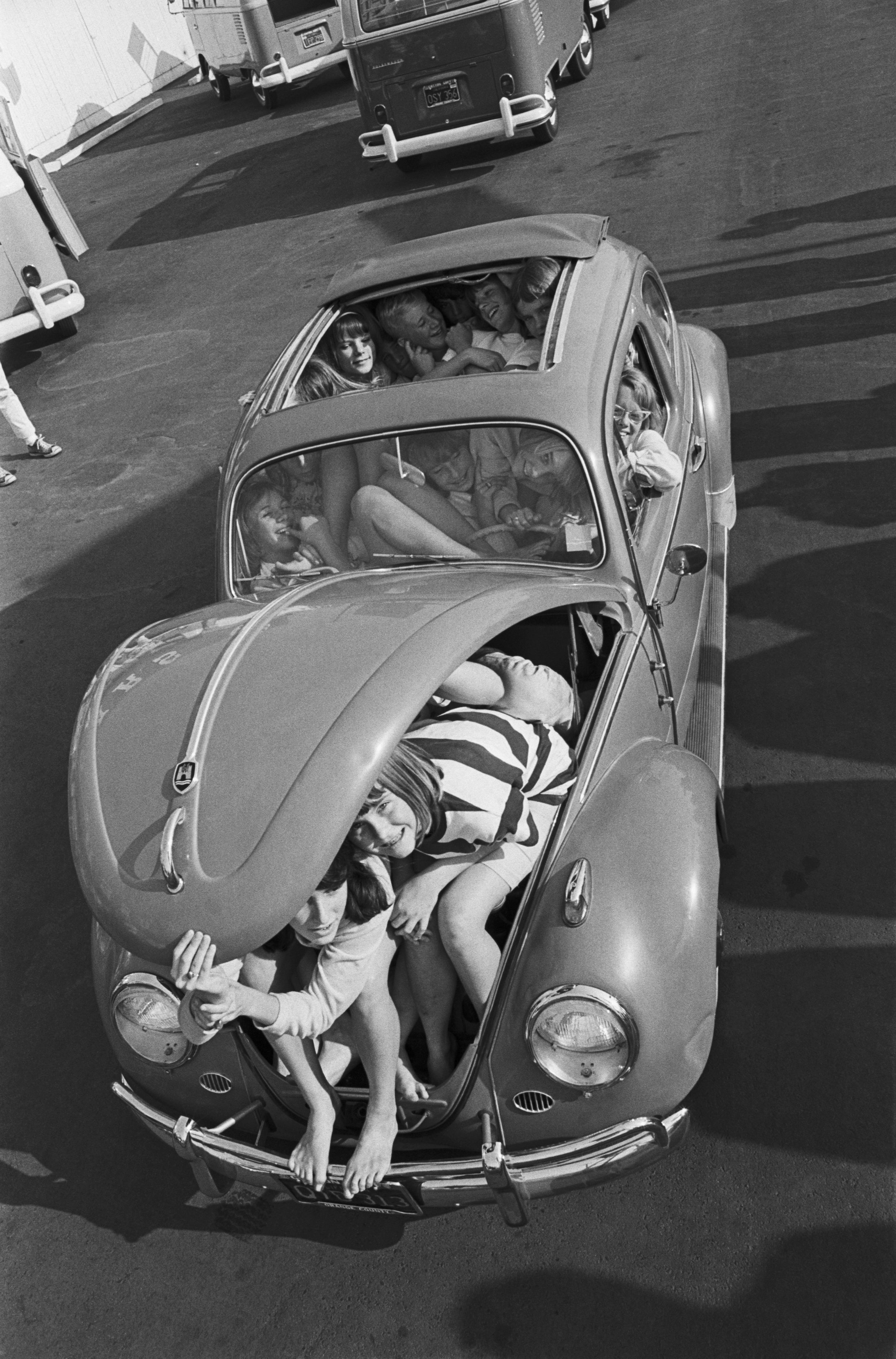 A radical  of radical   humorously squeezed into and onto an aged  Beetle car, with the beforehand   trunk unfastened  and showing legs and heads poking out
