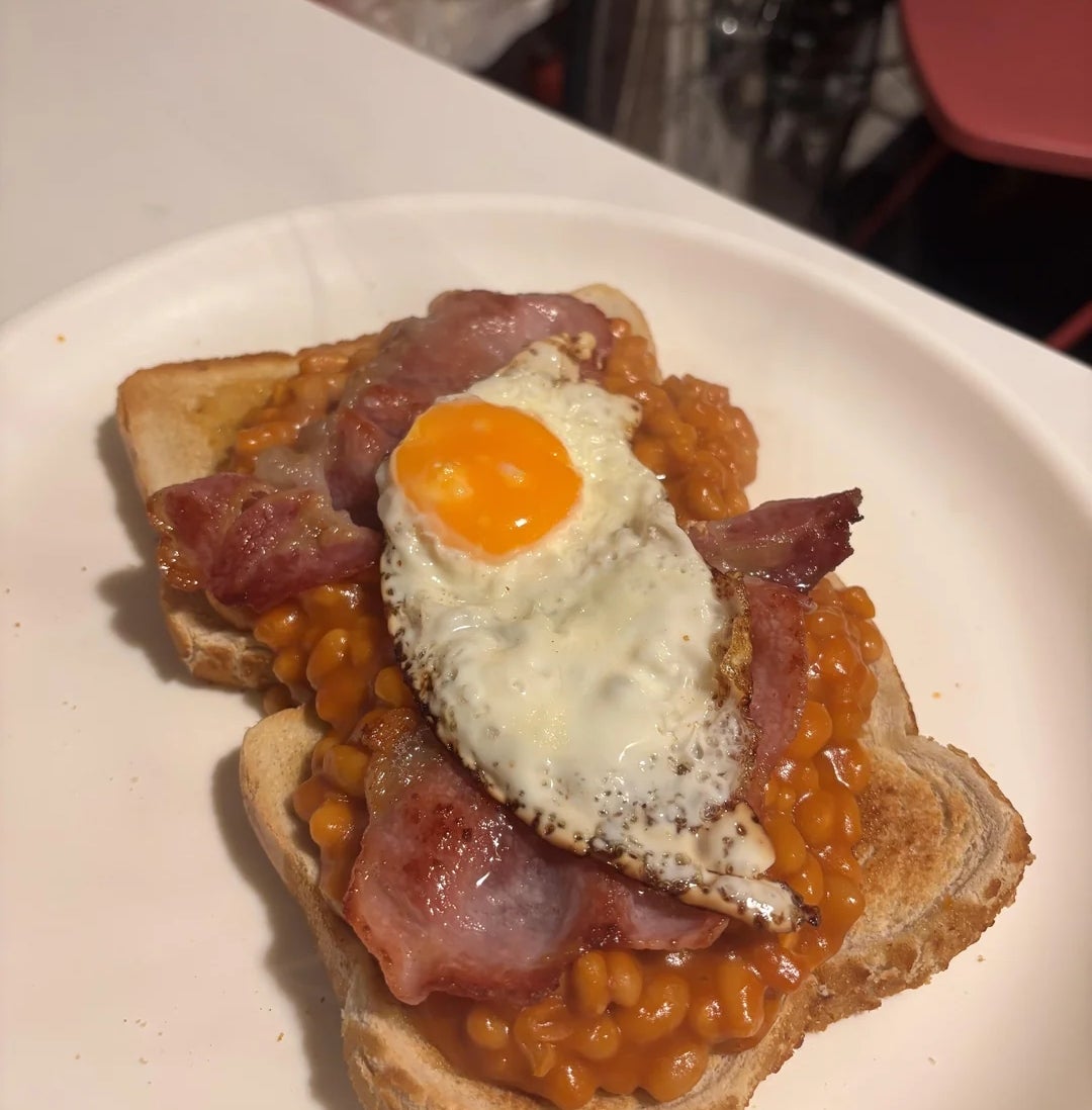 Sepotong roti panggang dengan kacang panggang, bacon, dan telur goreng di atas piring putih