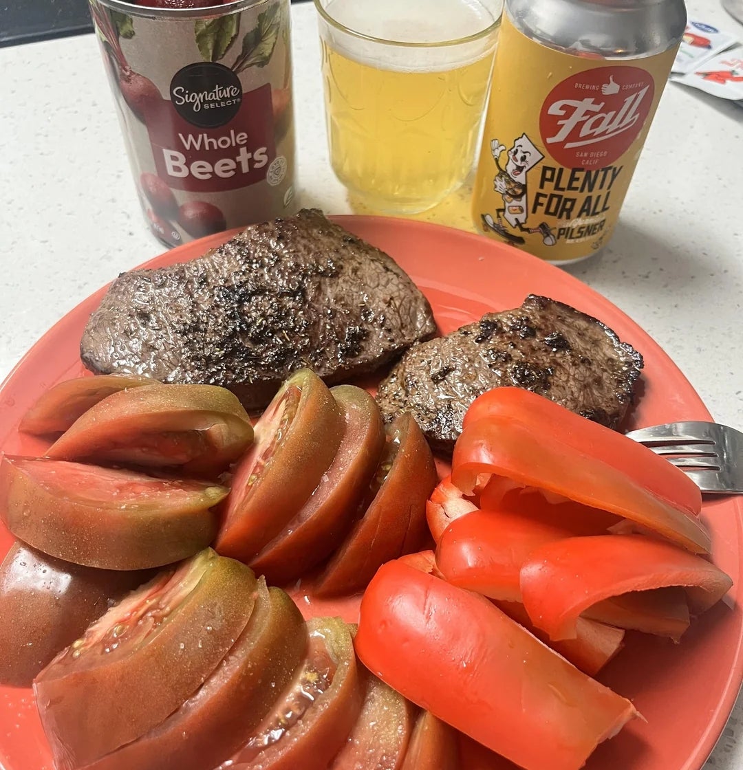 Piring dengan steak panggang dan irisan tomat dengan bit kalengan dan minuman di sampingnya