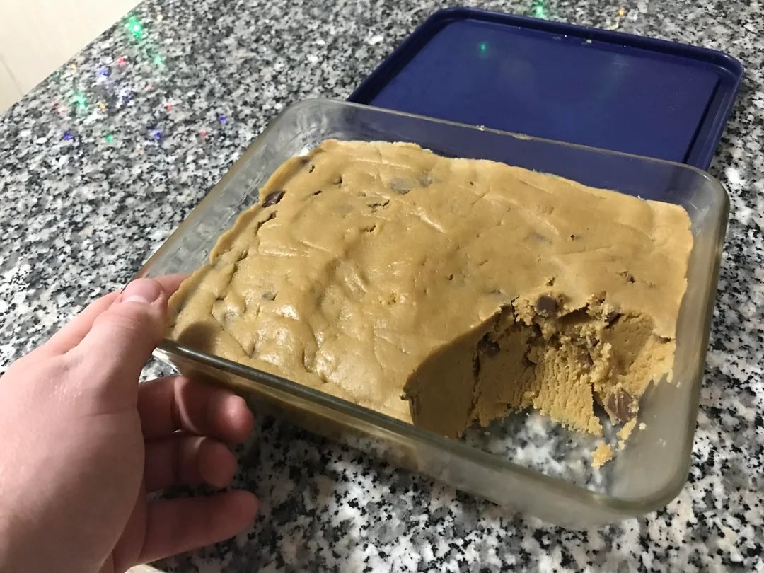 Piring kaca berisi adonan kue, dengan sebagian dikeluarkan, diletakkan di atas meja granit. Sebuah tangan memegang piring