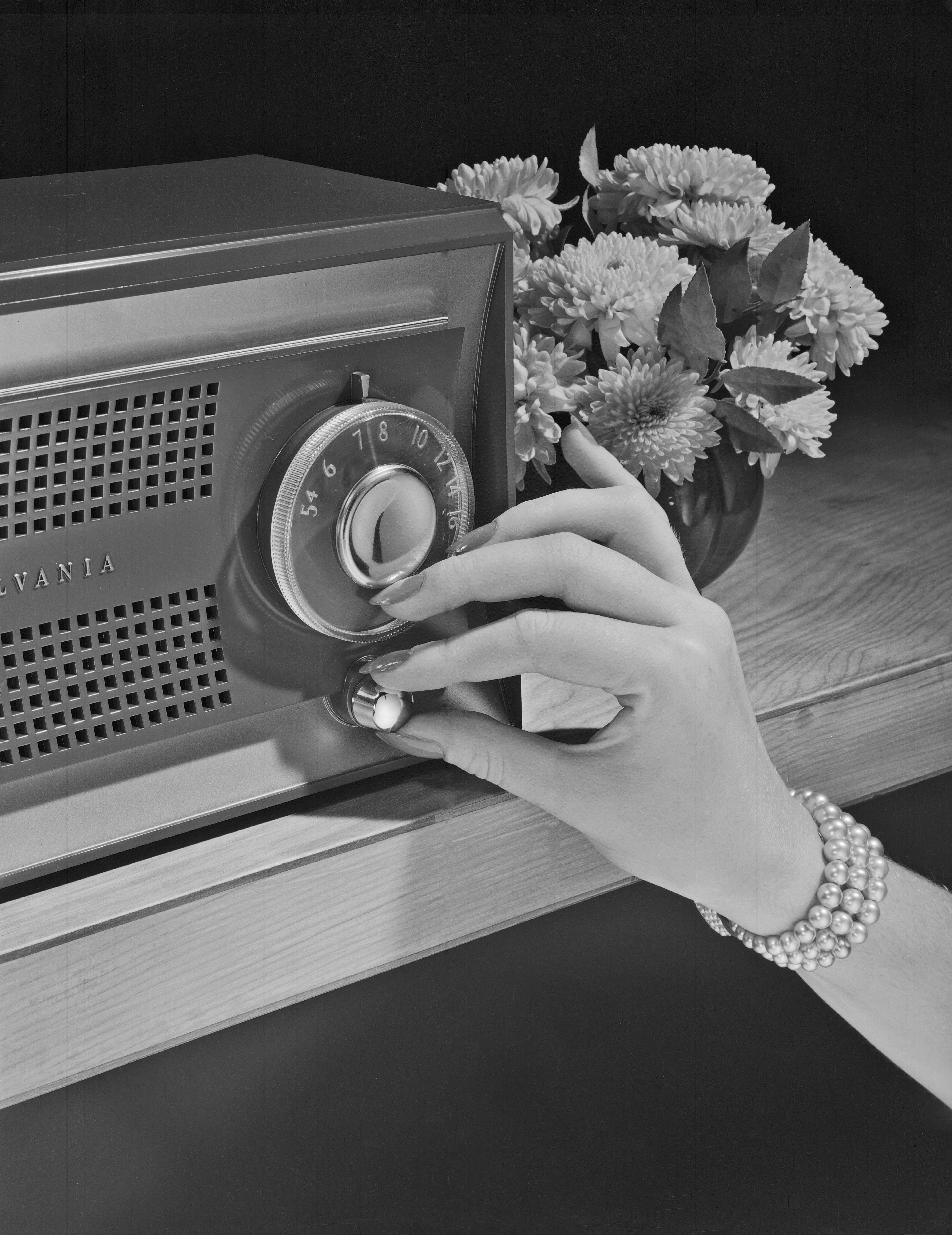 A manus  wearing a pearl bracelet tunes an old-fashioned vigor   connected  a woody  table, with flowers successful  the background