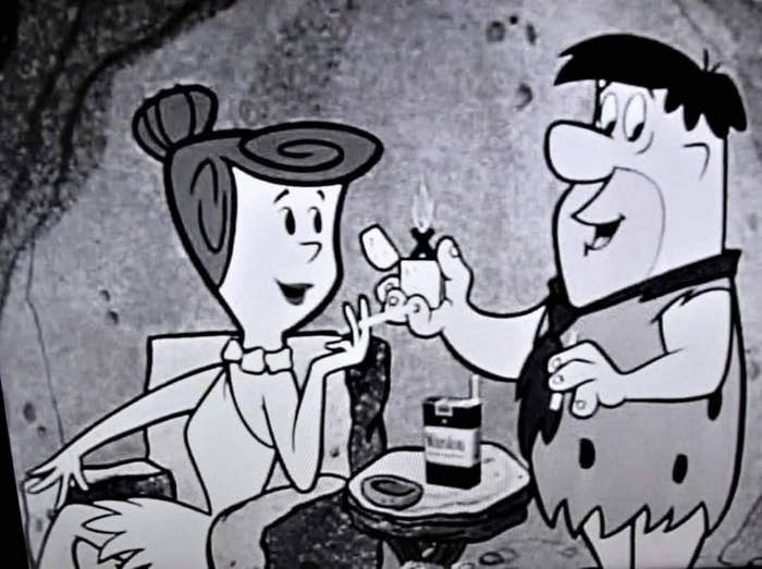 Wilma Flintstone and Fred Flintstone successful  a vintage cartoon country   with Fred offering a cigaret  to Wilma. 
