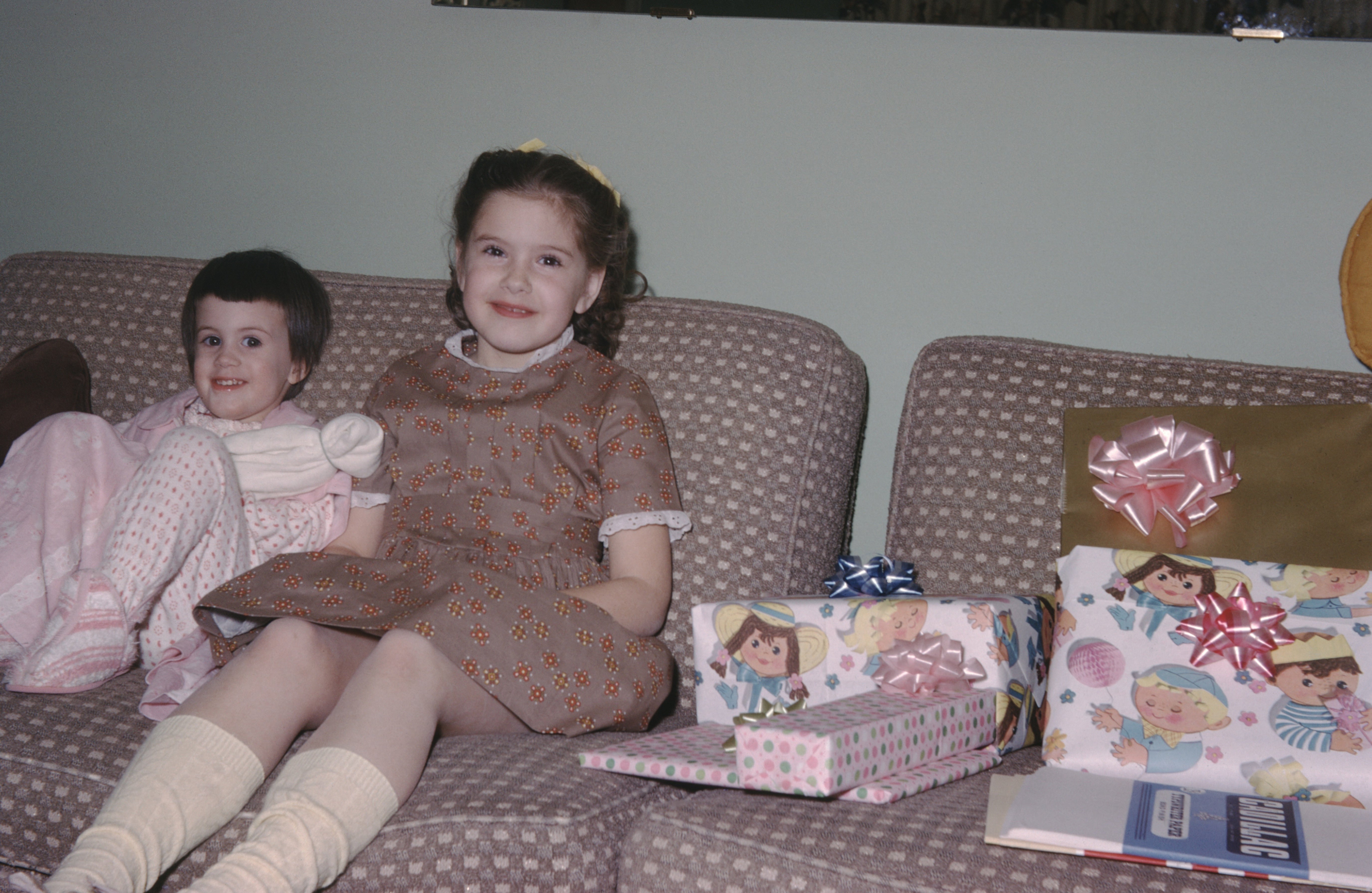 Two children beryllium   connected  a sofa  adjacent   wrapped gifts, smiling. They look  to beryllium  astatine  a solemnisation  oregon  party, perchance  a birthday