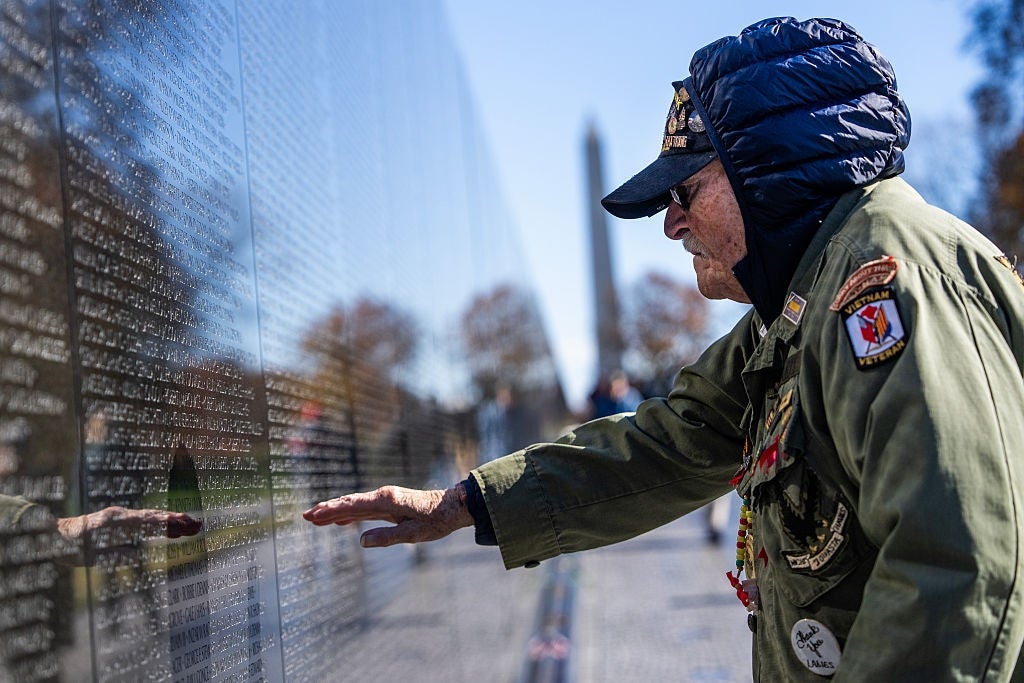 Elderly seasoned  successful  a decorated subject   overgarment   touches a reflective memorial partition  with engraved names