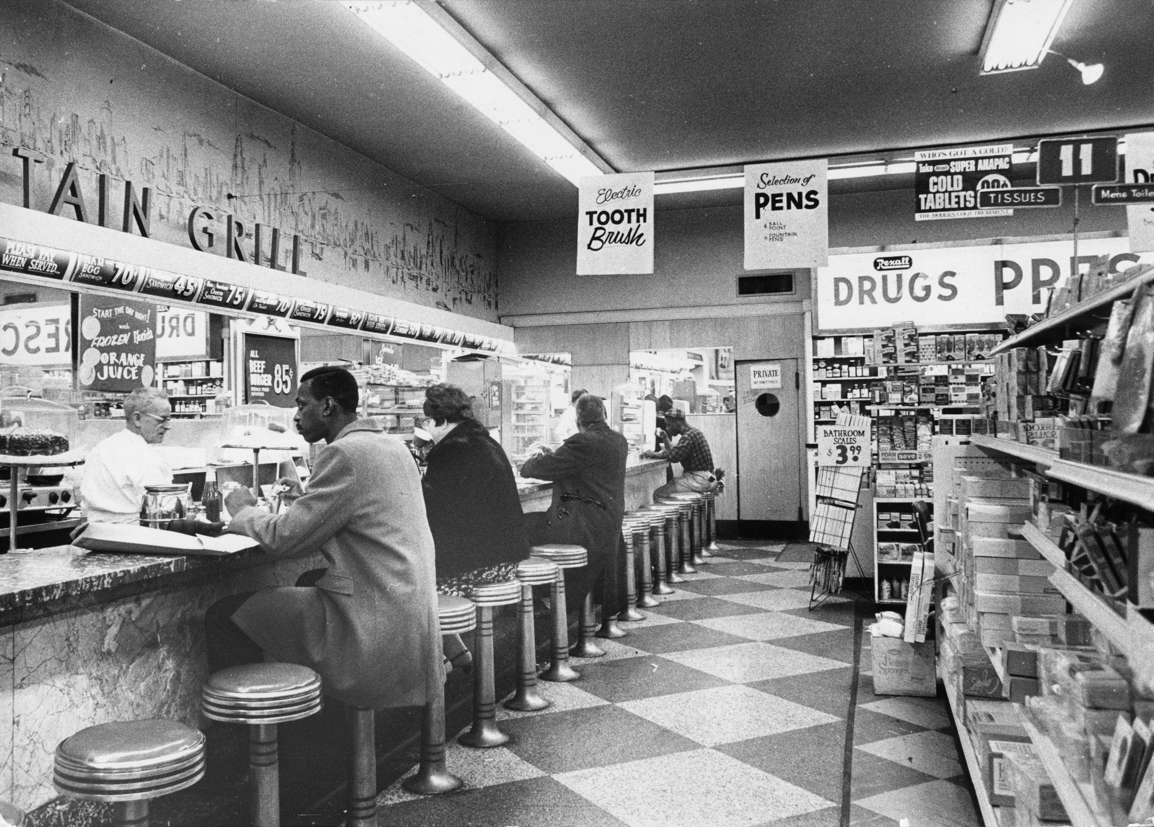 People seated astatine  a vintage diner antagonistic  wrong  a bustling drugstore, with shelves of products lining the close    side. 1950s setting