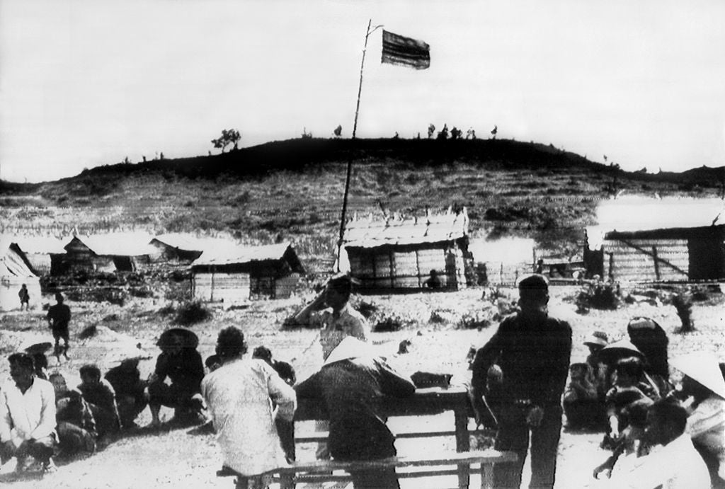 Historical representation  of a radical  of radical   sitting outdoors adjacent   makeshift structures with a emblem  connected  a pole