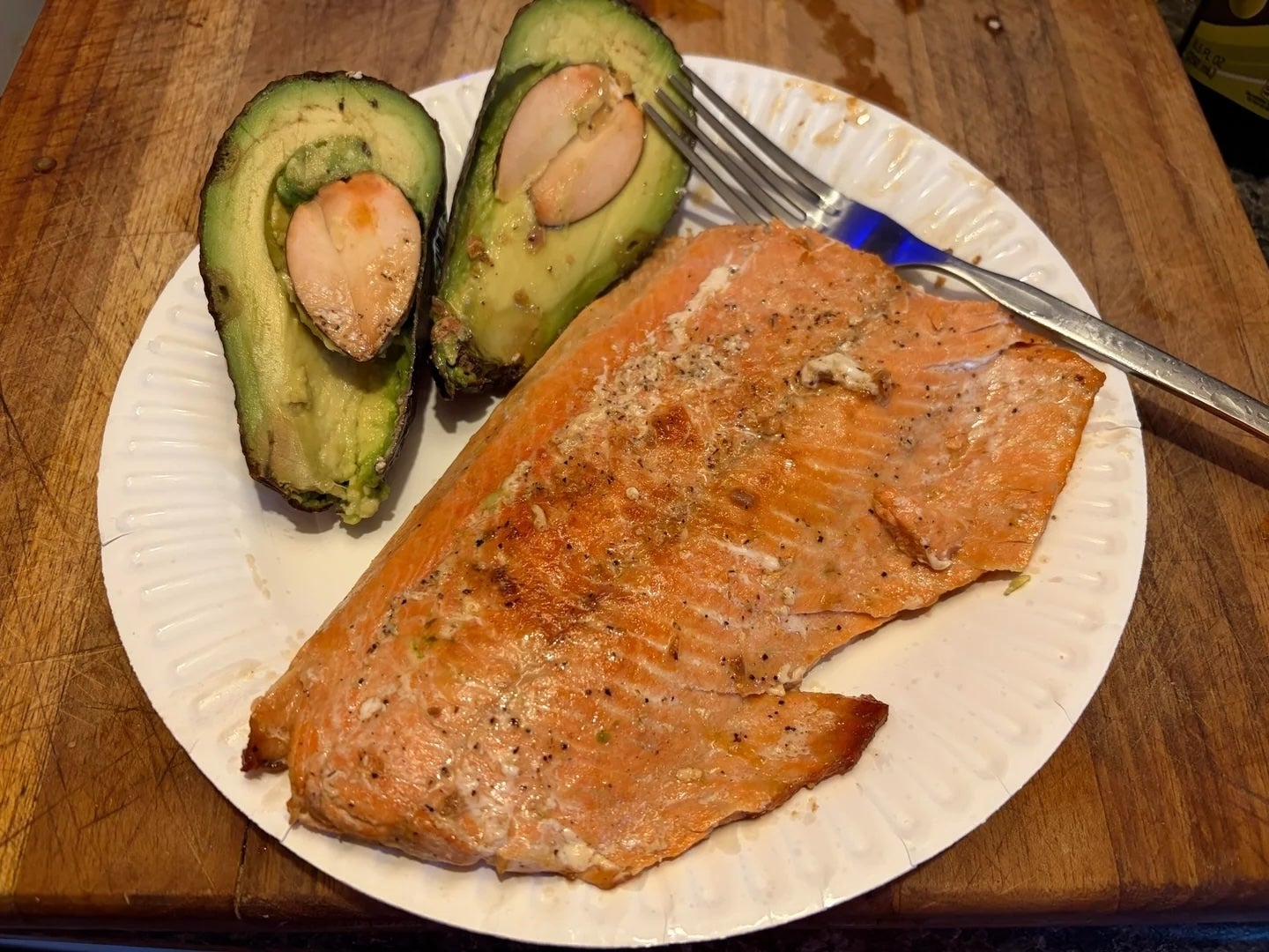 Fillet salmon panggang di piring dengan garpu, disajikan bersama alpukat yang dibelah dua