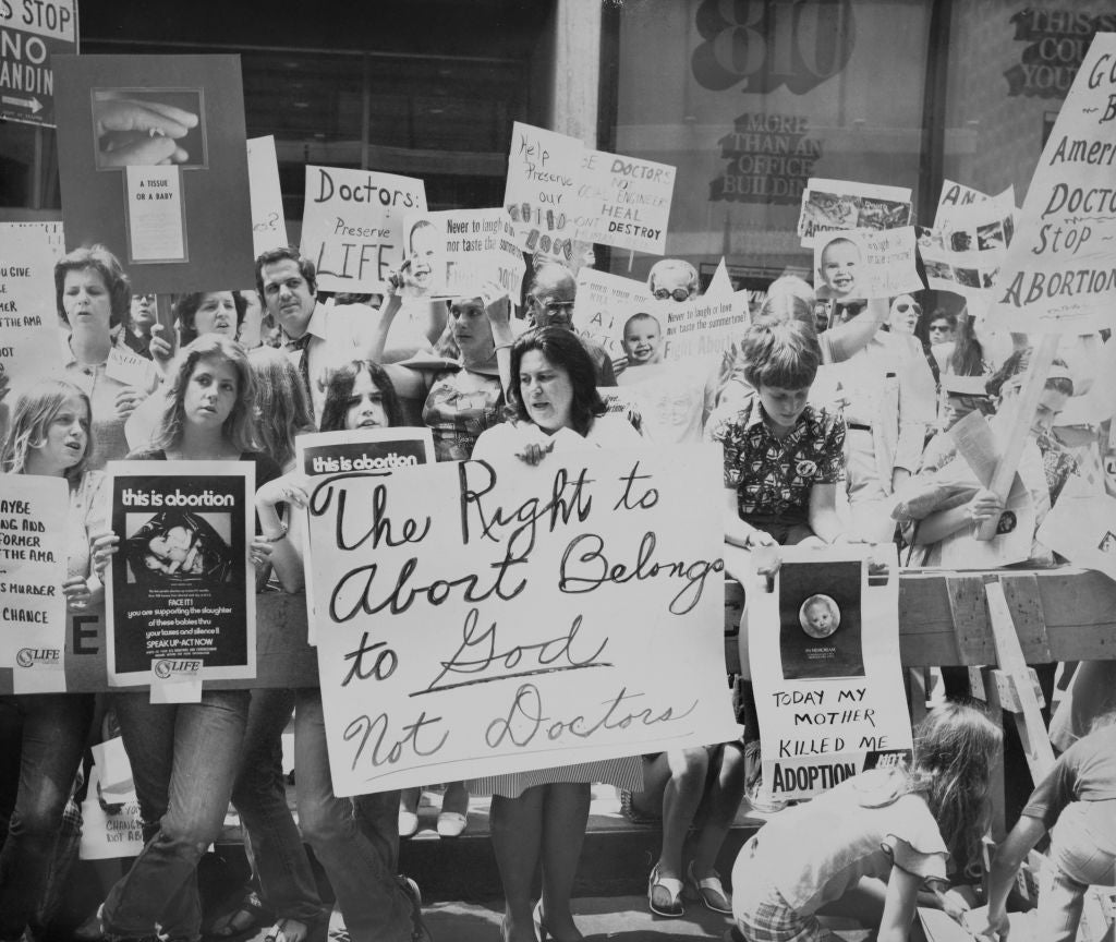 A black-and-white photograph  of an anti-abortion protestation  with radical   holding signs, including 1  that reads, "The Right to Abort Belongs to God, Not Doctors."