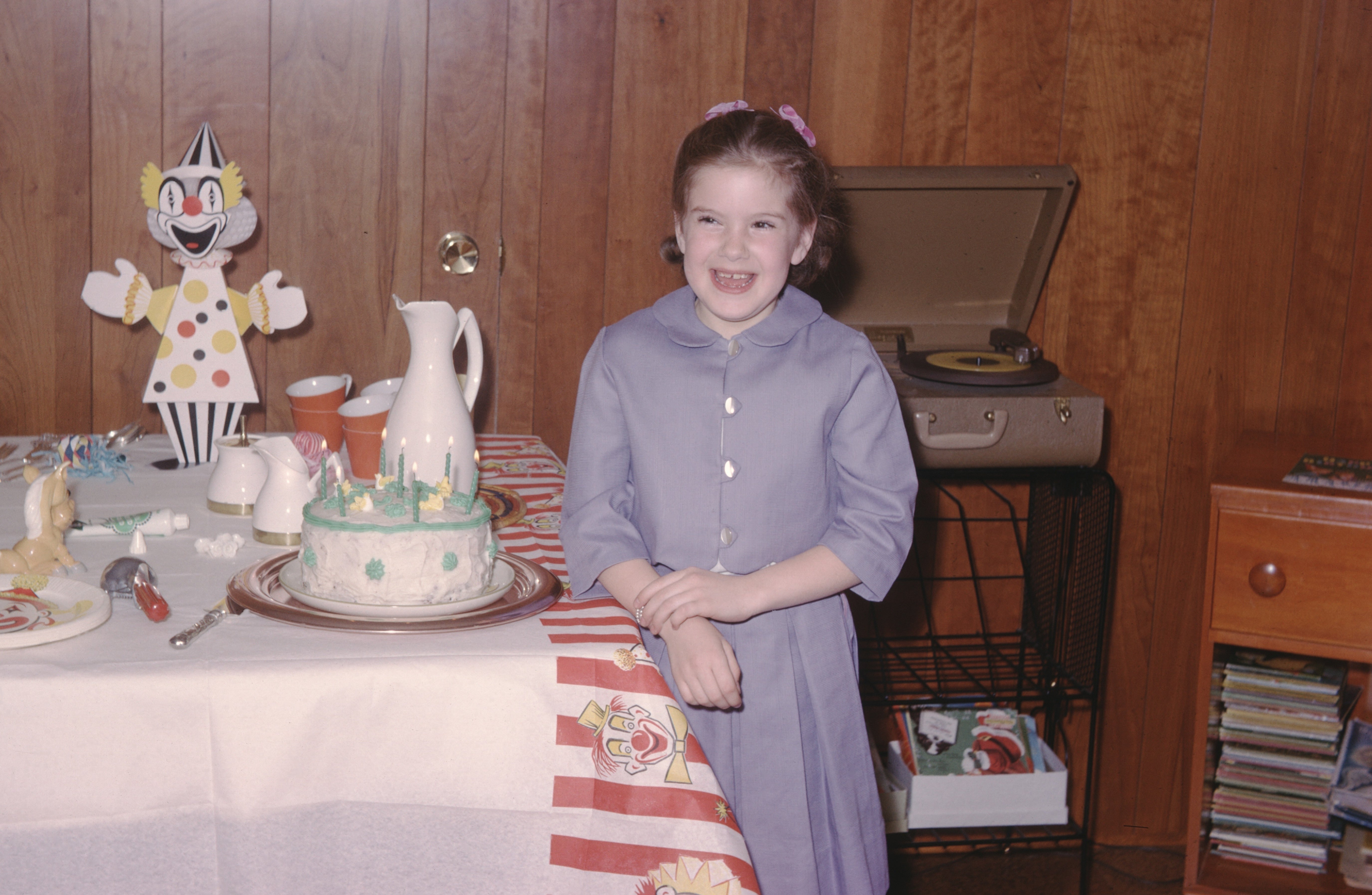 A young miss  successful  a vintage formal  stands beside a day   barroom   connected  a table, with a grounds   subordinate    and cartoon decorations successful  the background