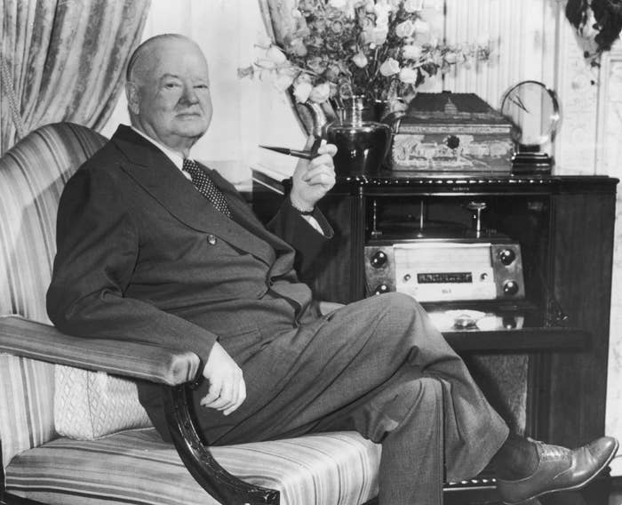 A antheral   successful  a suit   sits successful  an armchair, holding a pipe, adjacent  to a vintage vigor   and floral arrangement