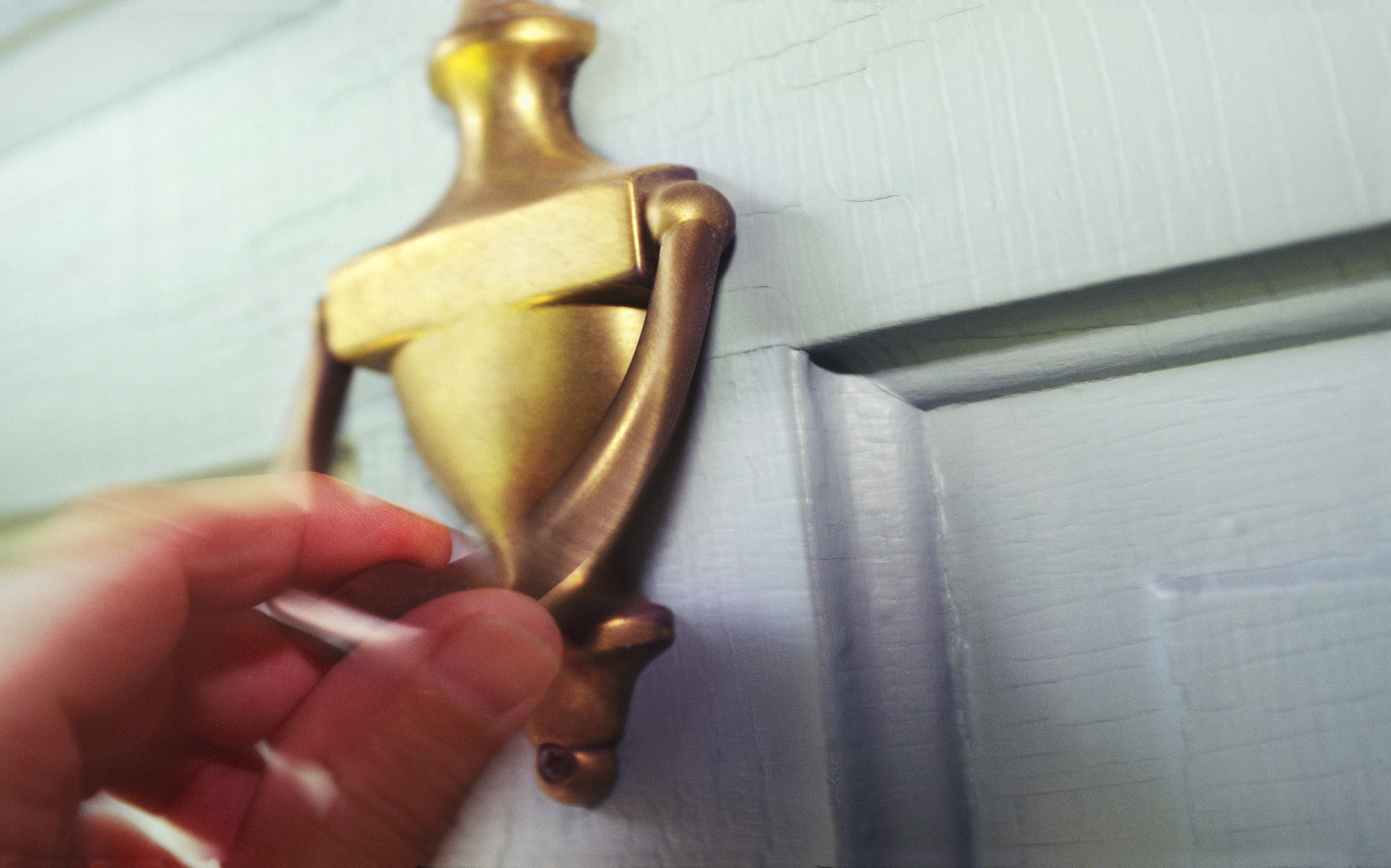 Hand reaching towards a brass doorway  knocker connected  a woody  door