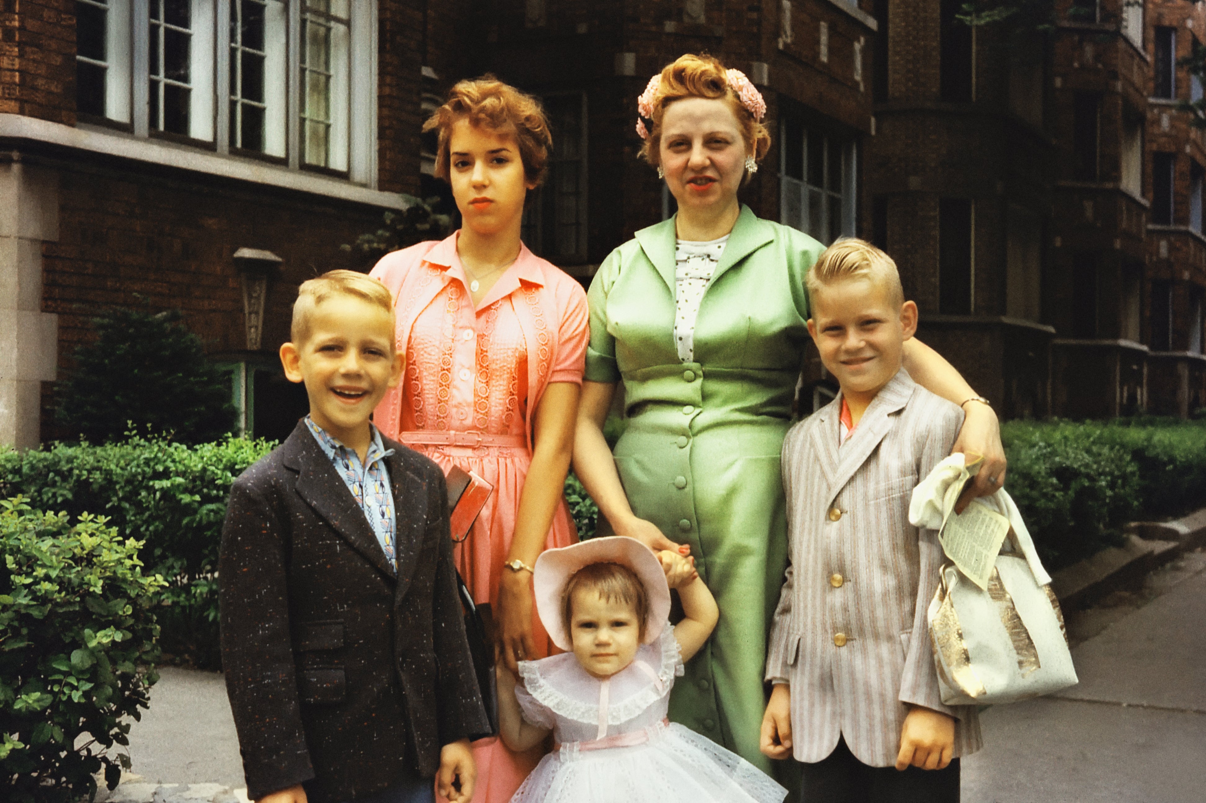 Familieportrett utenfor, med to kvinner i vintagekjoler og tre barn, en i dress og den yngste i kjole og panser