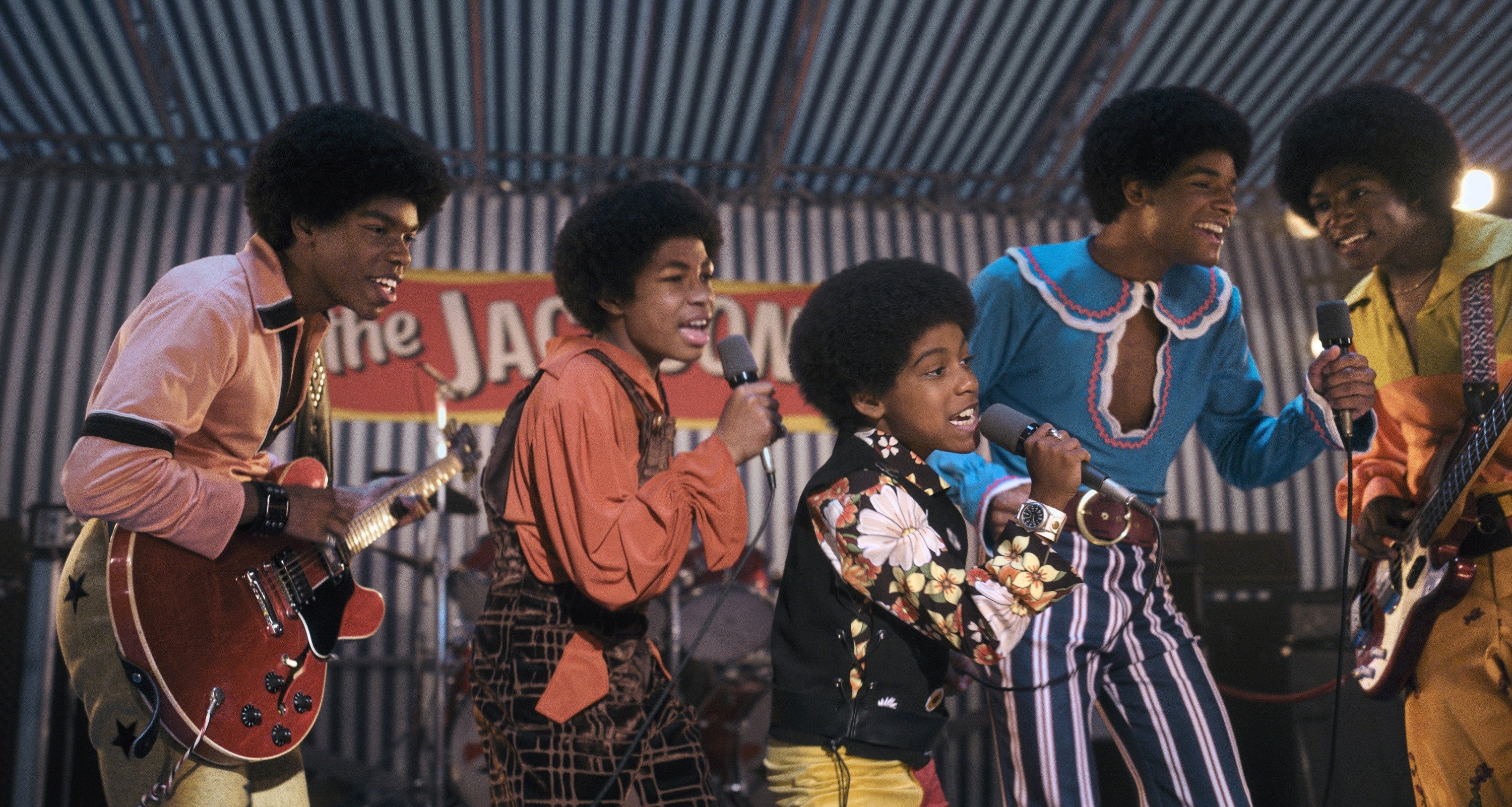A radical  performs connected  stage, wearing vibrant, retro-style outfits with afros, singing and playing instruments energetically