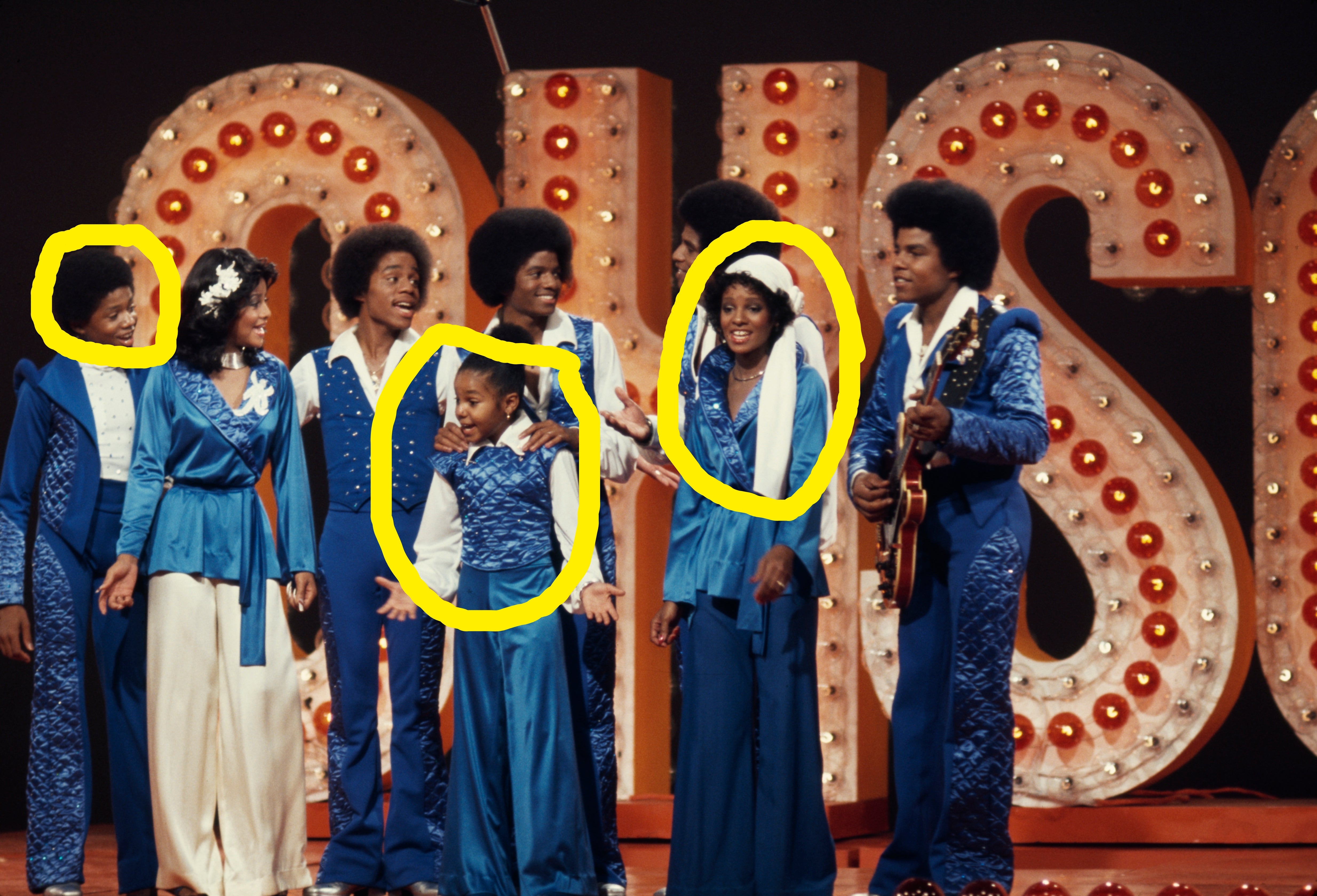 A radical  of performers connected  signifier    successful  coordinated, vibrant outfits reminiscent of 70s fashion, with immoderate   holding instruments, successful  beforehand   of a ample  lit sign