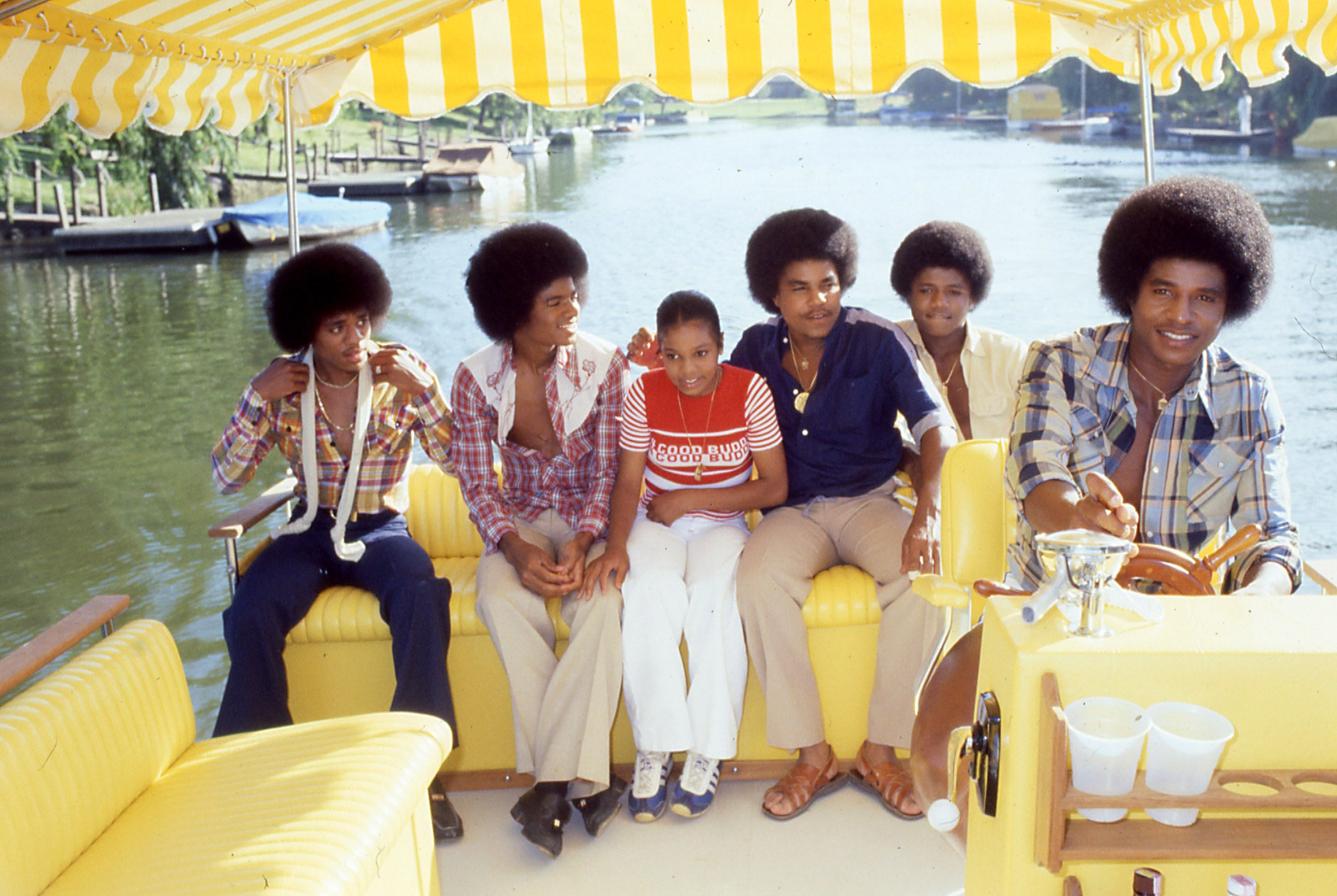 Group of six radical   sitting connected  a vessel  with a yellowish  canopy, dressed successful  1970s casual attire, smiling and enjoying a leisurely infinitesimal   connected  the water