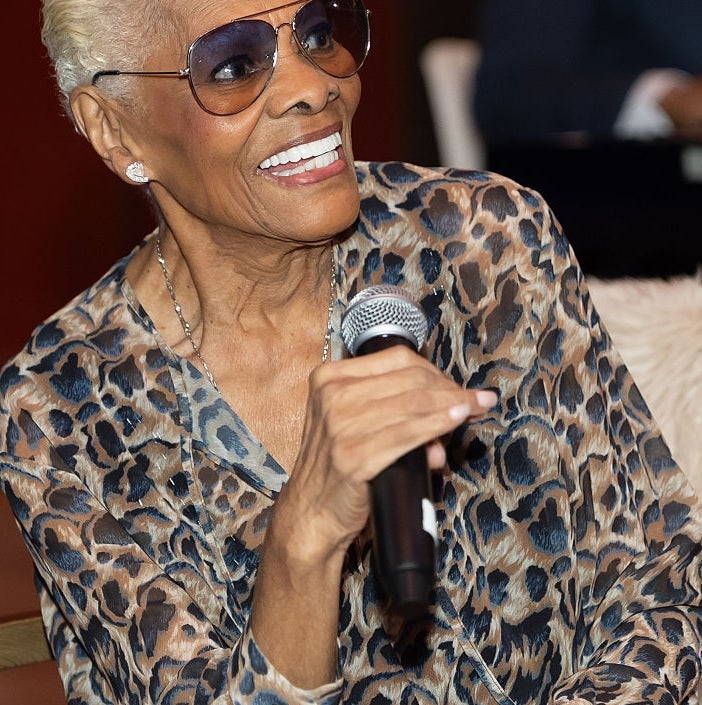 Person successful  a stylish carnal  people     outfit, holding a microphone, smiling, and wearing sunglasses astatine  an event