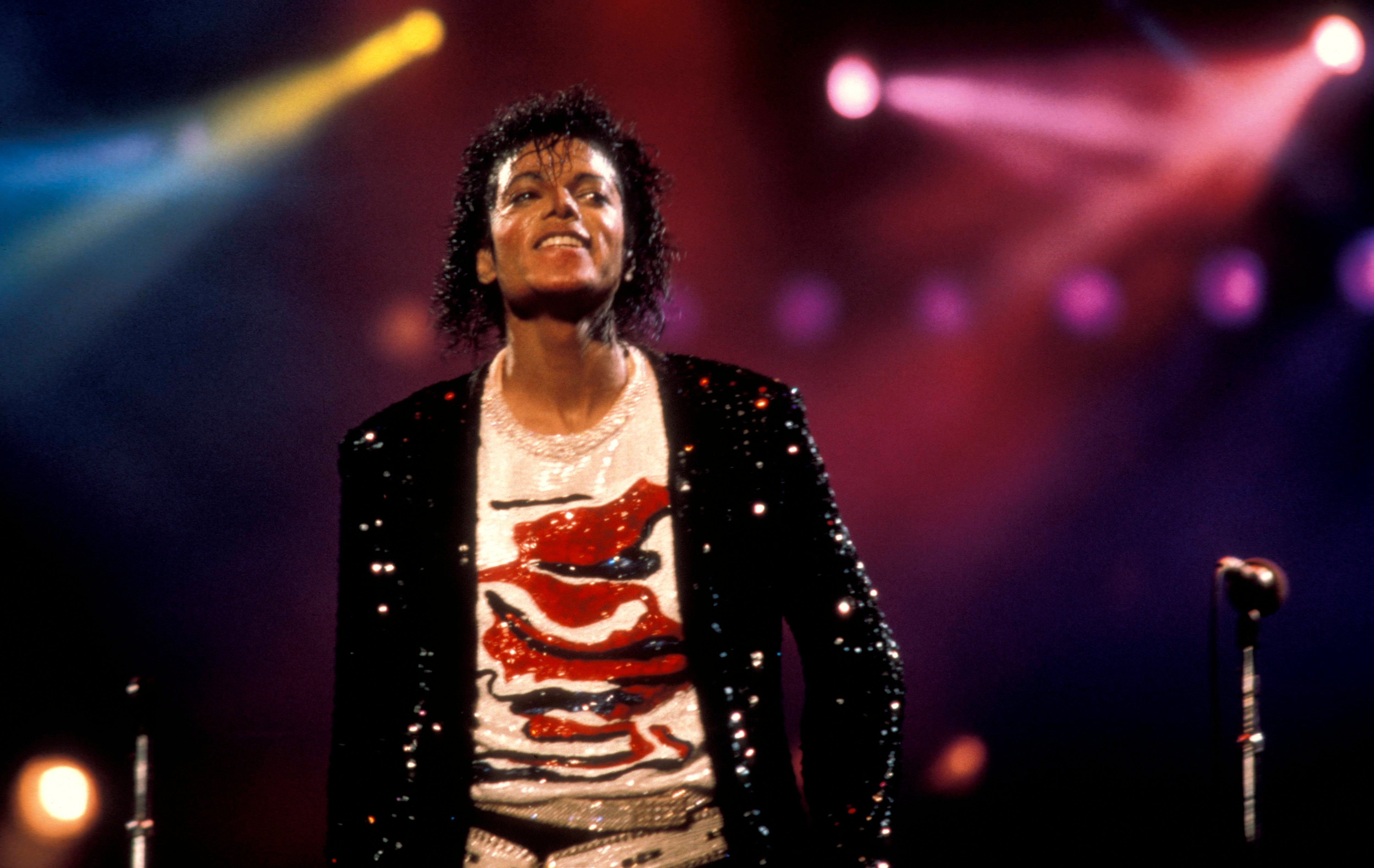 Singer performing connected  signifier    successful  a sequined overgarment   and graphic T-shirt, with signifier    lights successful  the background