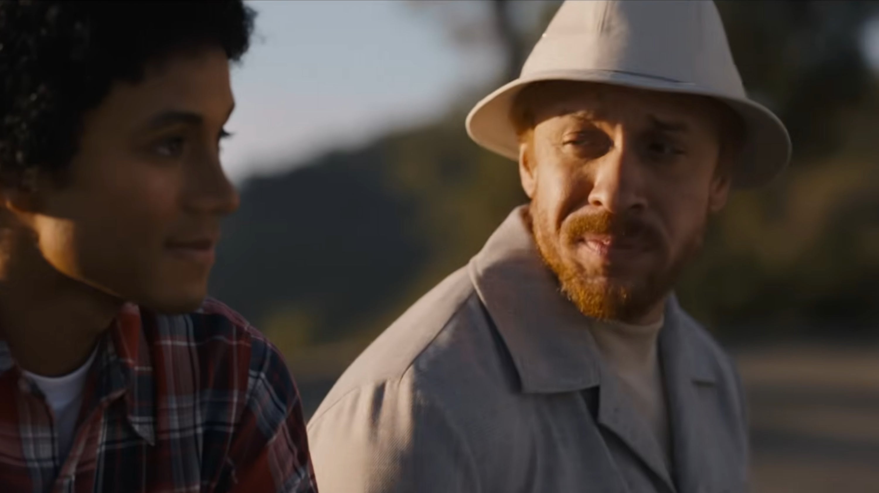 Two radical   sitting outdoors, 1  successful  a plaid garment  and the different   successful  a airy  overgarment   and hat, engaged successful  a conversation