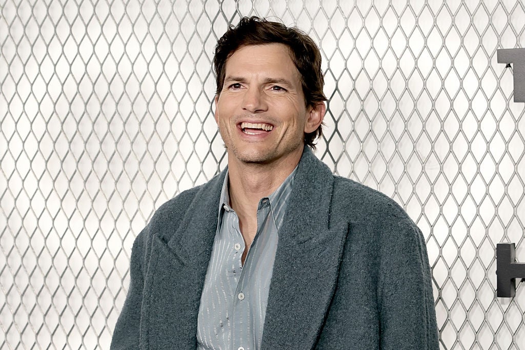 Person smiling, wearing a grey  overgarment  implicit    a striped shirt, lasting  successful  beforehand   of a patterned background