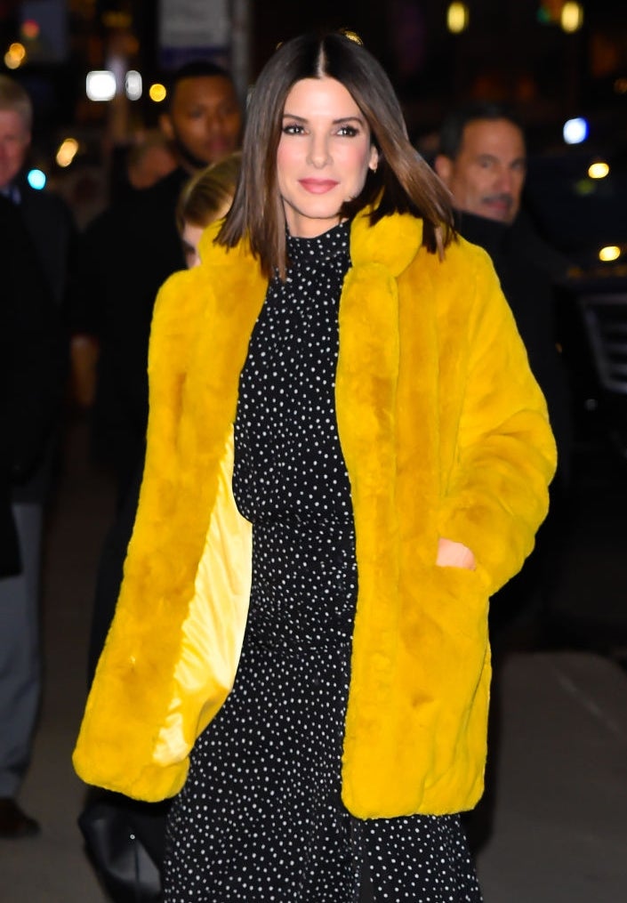 A pistillate   wearing a achromatic  polka dot formal  and a yellowish  overgarment  walks confidently astatine  a nationalist   event