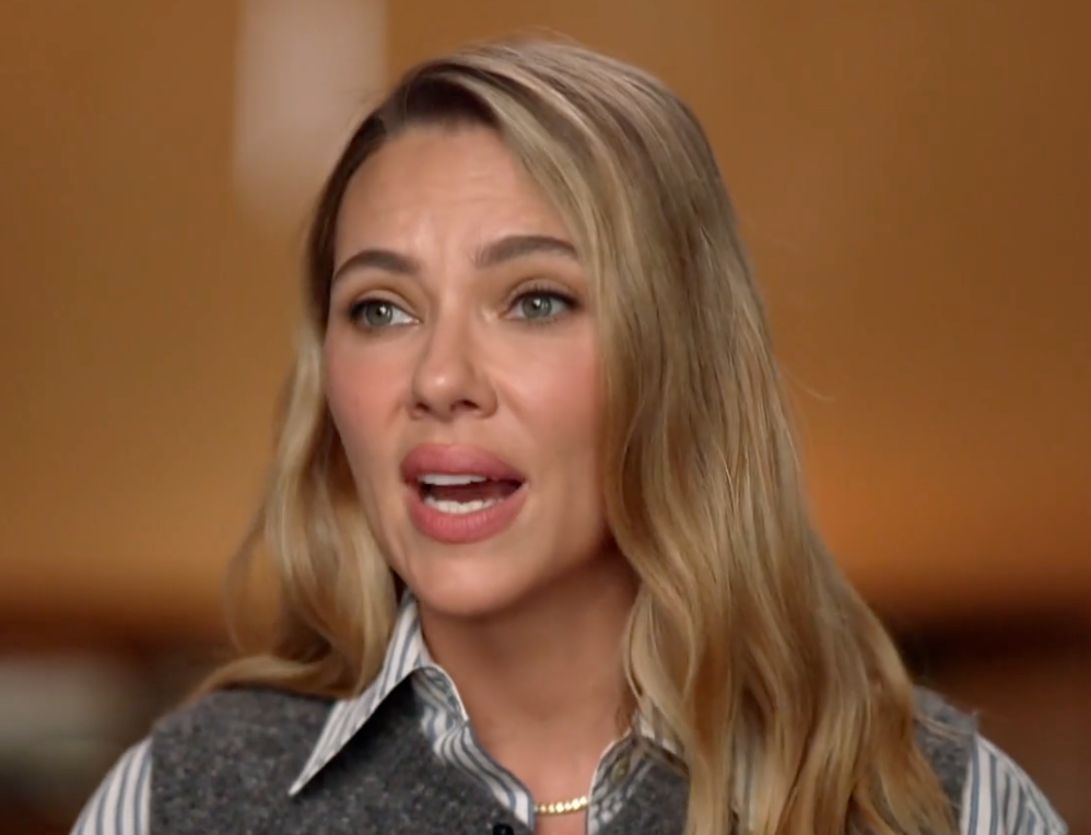 Person speaking during an interview, wearing a striped collared garment  and a vest, outdoors
