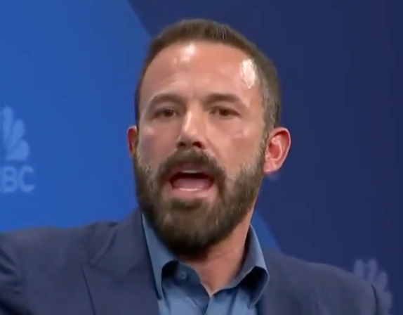 A idiosyncratic   successful  a suit   speaks animatedly astatine  an event, appearing engaged successful  the discussion