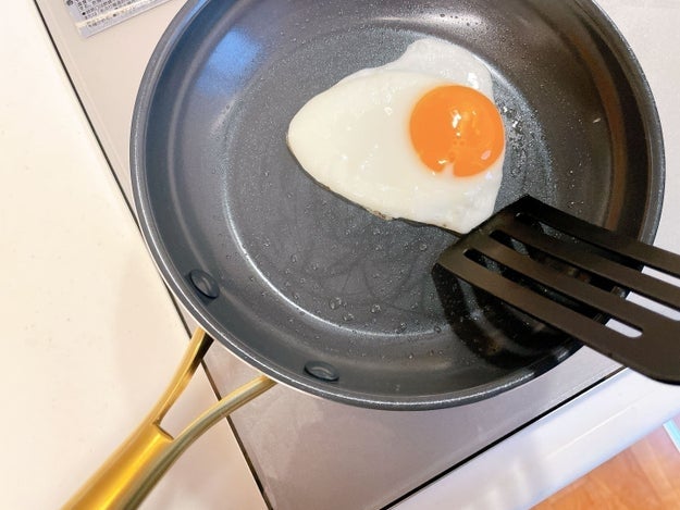 フライパンで片面が焼かれている目玉焼き。プラスチック製のフライ返しが見えている。