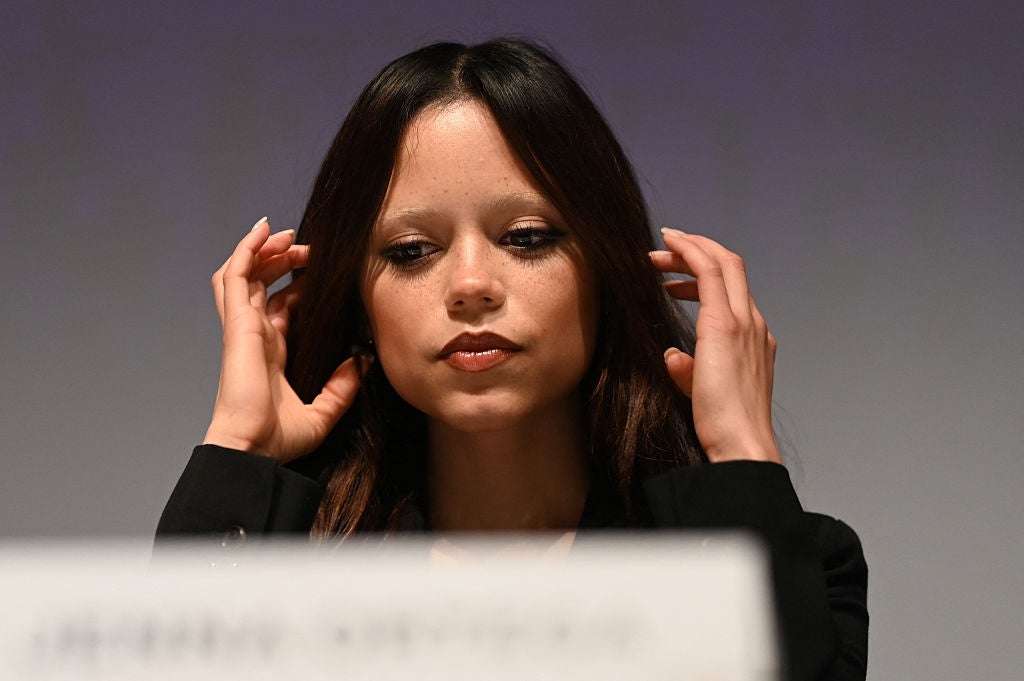 A idiosyncratic   is seated, adjusting their hair, wearing a acheronian  blazer, astatine  what appears to beryllium  a ceremonial  lawsuit   oregon  property   conference